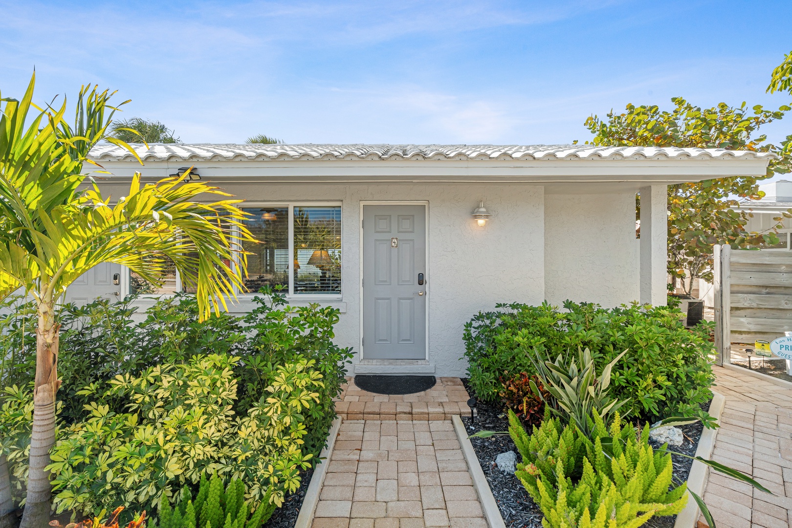 Charming single-story vacation home with tropical landscaping and tile roof, surrounded by lush palm trees and manicured gardens in a peaceful residential setting.
