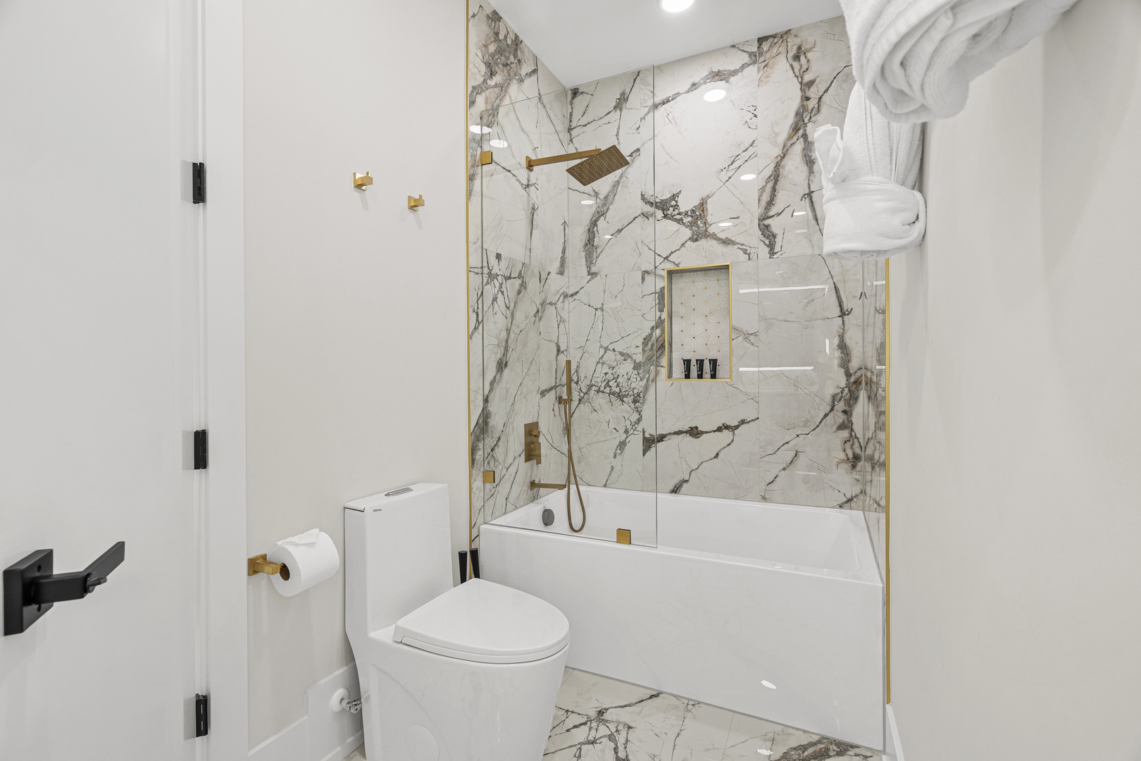 Step into your luxurious marble-adorned bathroom, where elegant gold fixtures and a pristine soaking tub create your personal spa retreat. Fresh towels await your arrival.