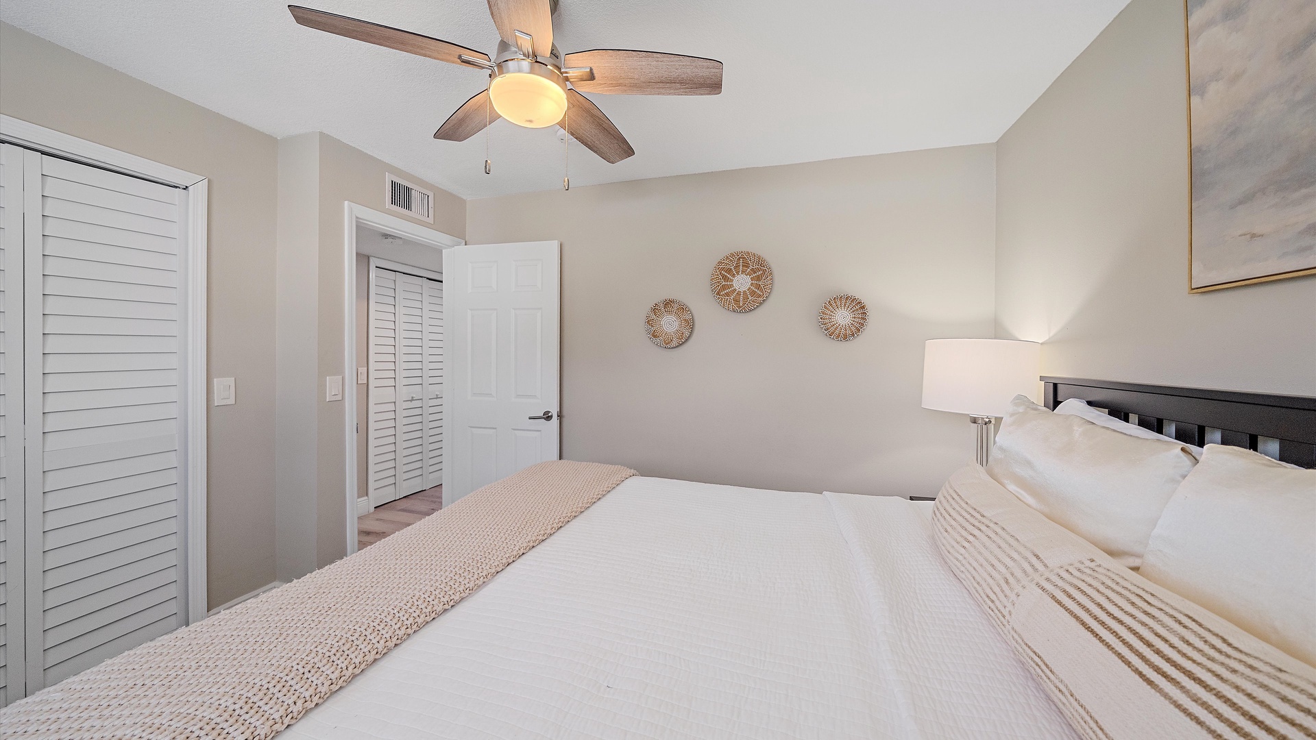 Sink into crisp linens and coastal calm in your serene bedroom, where soft tones and gentle ceiling fan breezes invite deep, restful sleep.
