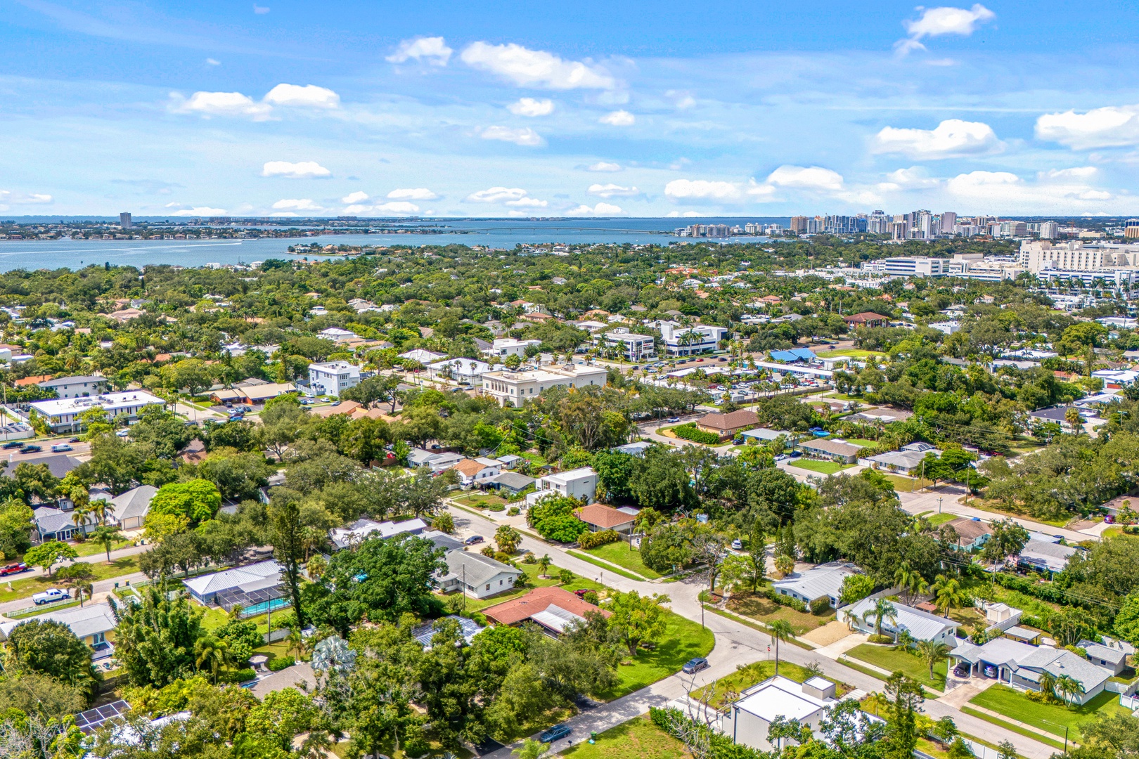 Aerial view showcasing a lush residential neighborhood nestled between bay waters and the city skyline, offering a tranquil retreat with easy access to urban amenities.