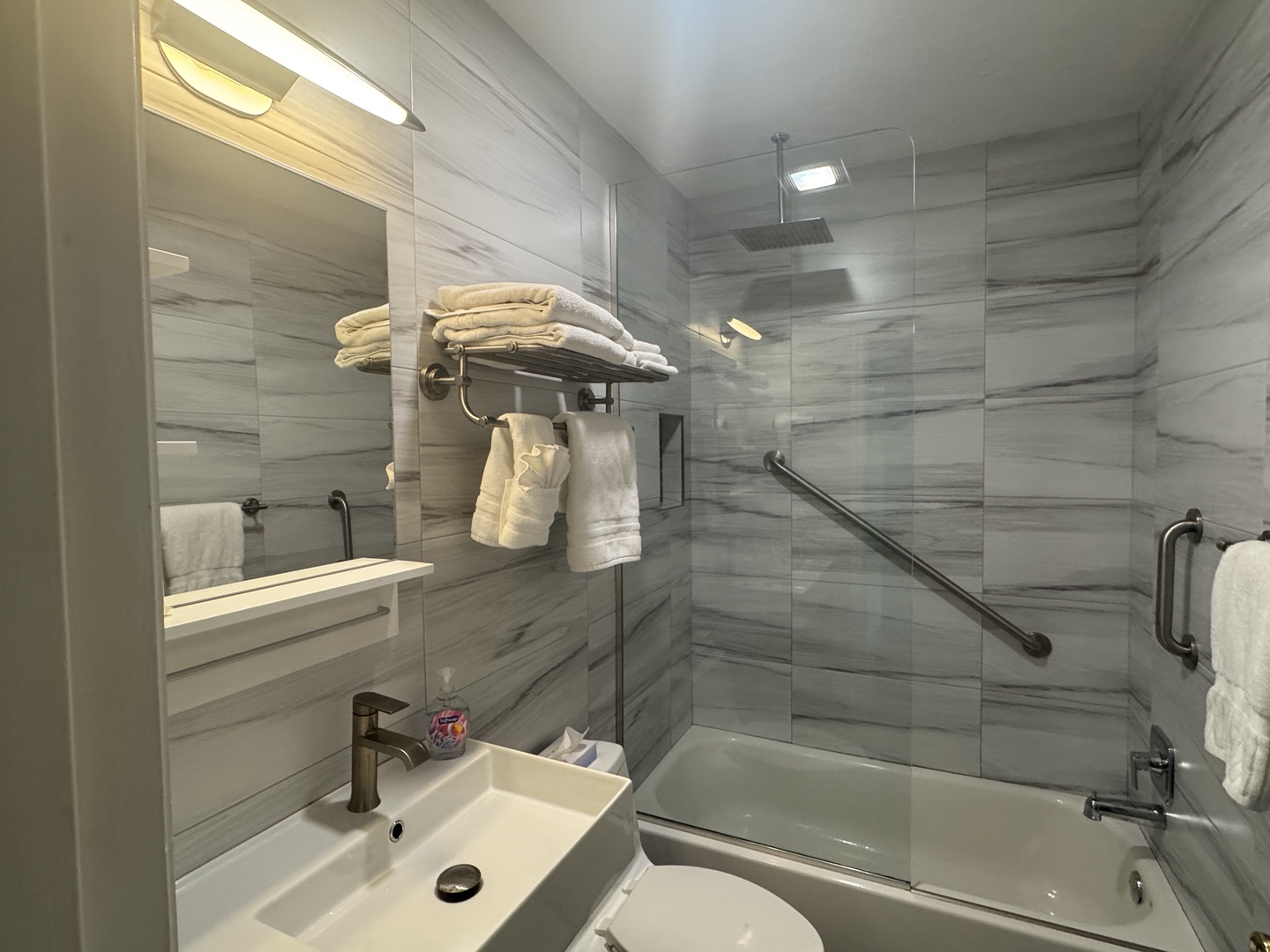 A modern bathroom with sleek gray tiling and fresh towels ready for your arrival. Enjoy your rain showerhead and convenient grab bars after a day of exploring.
