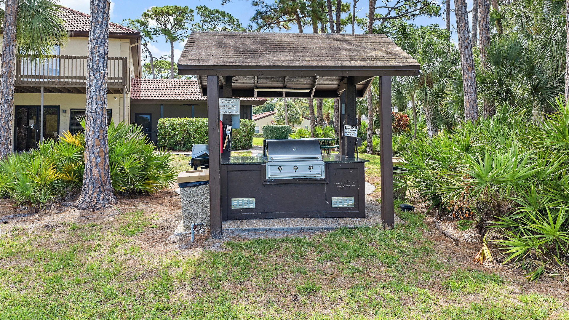A covered grilling station nestled among tropical palms and pines, offering a peaceful spot for outdoor cooking and gatherings near the property.