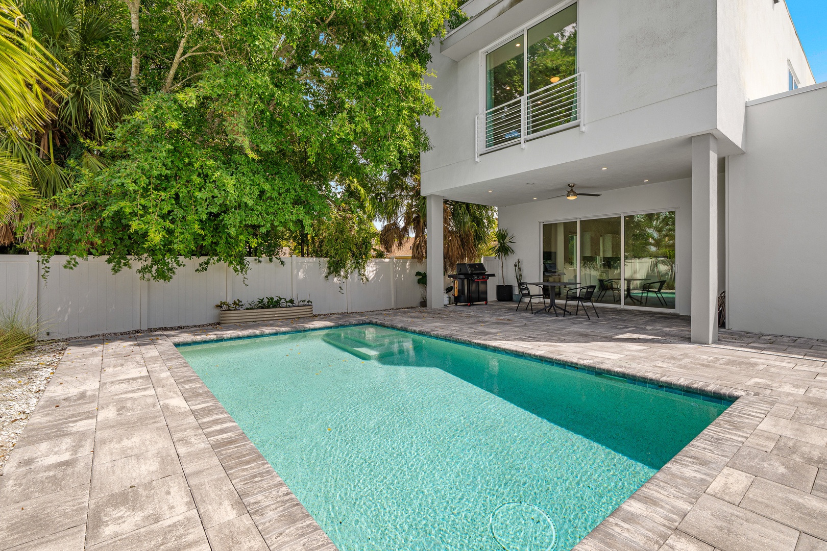 A modern two-story home with a private pool, outdoor dining patio, and lush tropical landscaping in a quiet backyard setting.