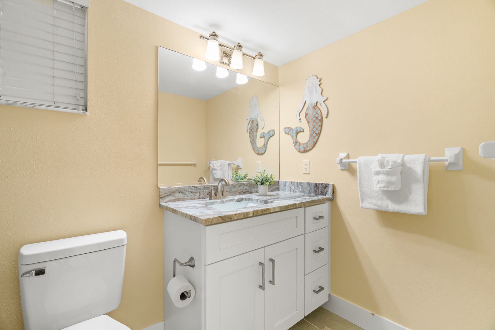 Your bright bathroom features coastal charm with mermaid decor, granite counters, and fluffy towels ready for your stay.