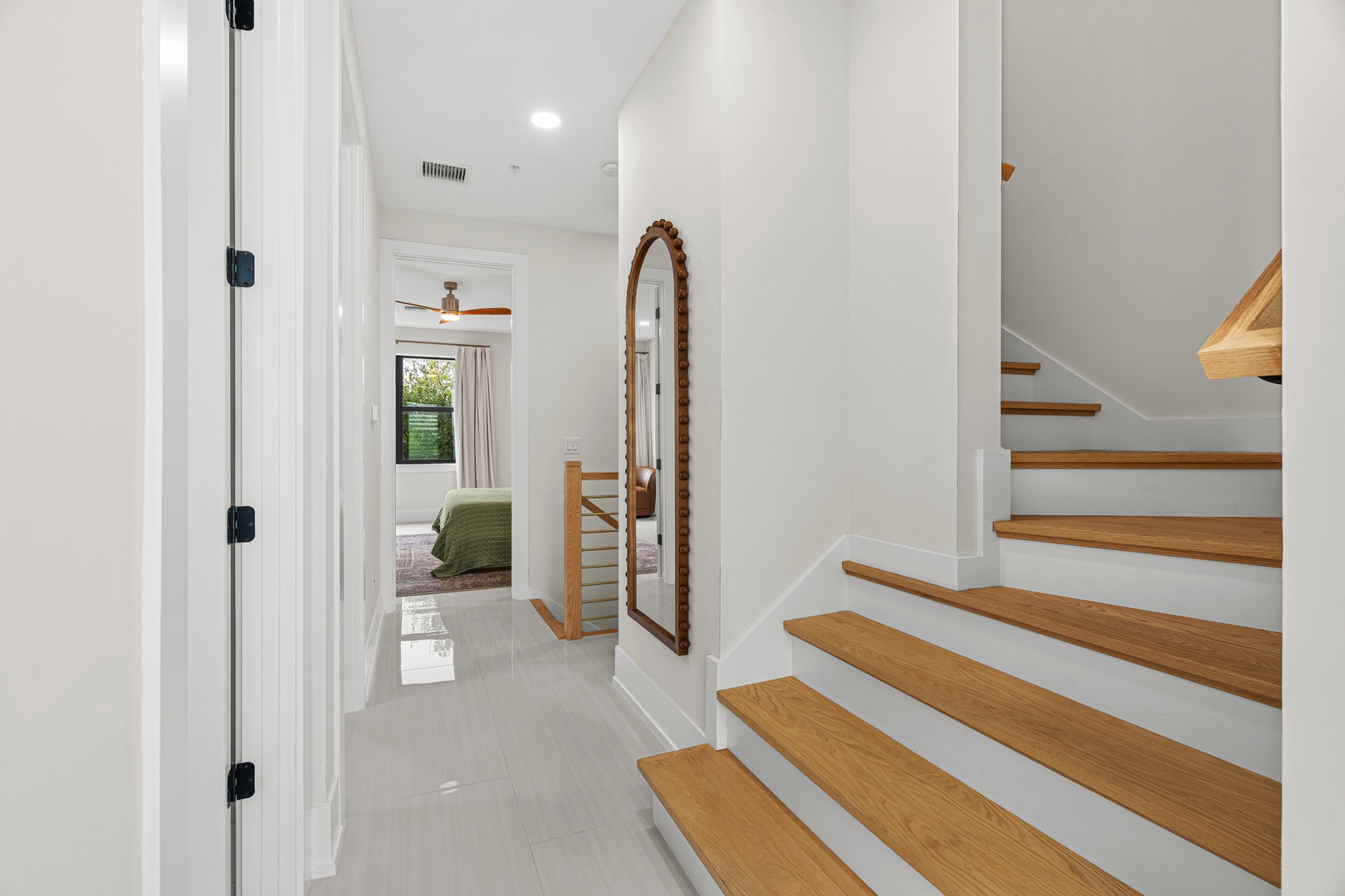 Bright hallway leading to your bedroom, featuring warm wood stairs and a charming full-length mirror. The ceiling fan and natural light make this space feel airy and welcoming.