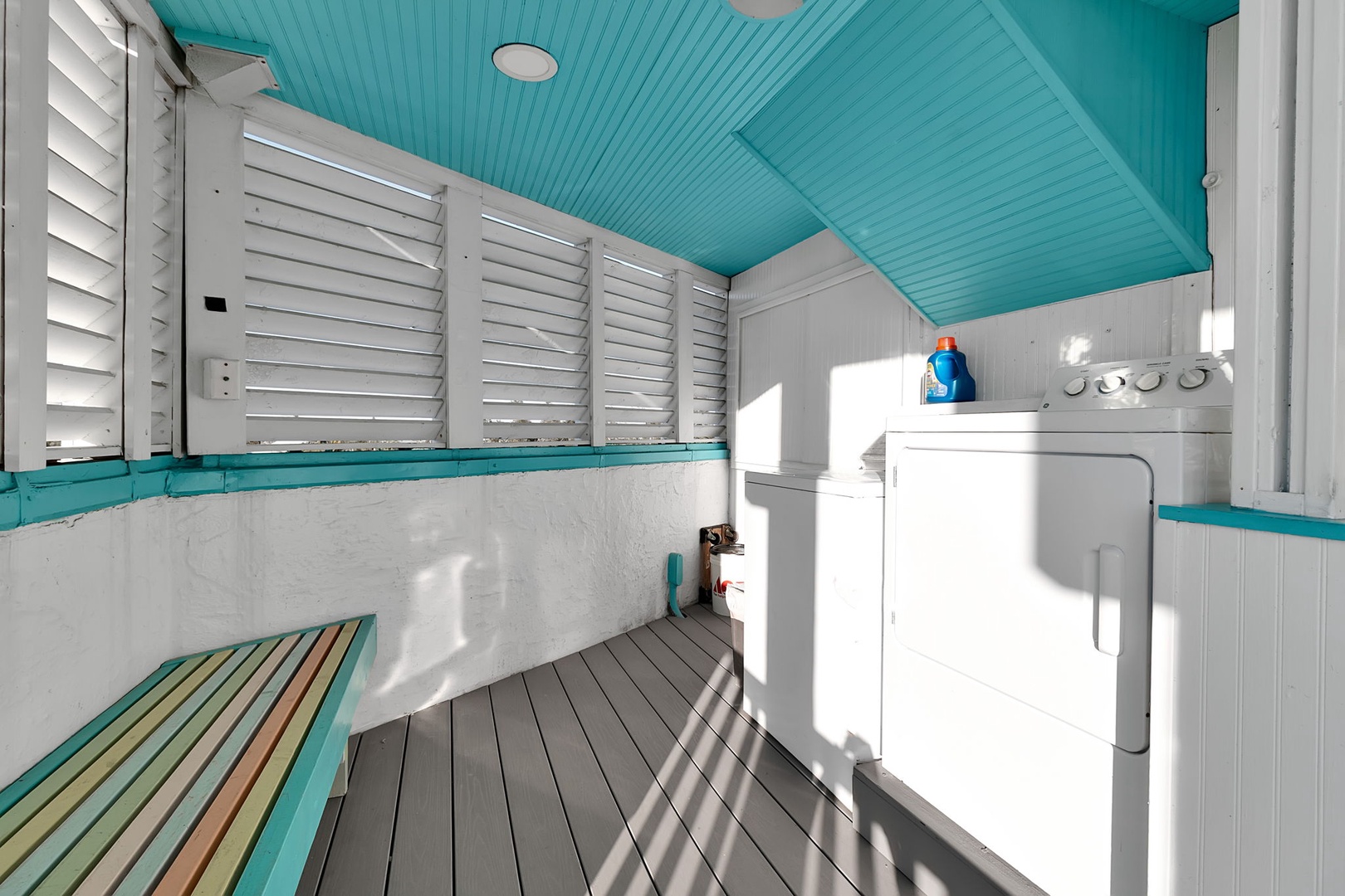 Charming outdoor shower with vibrant turquoise ceiling, coastal white shutters, and colorful deck floor—the perfect post-beach rinse spot with natural light and tropical flair.
