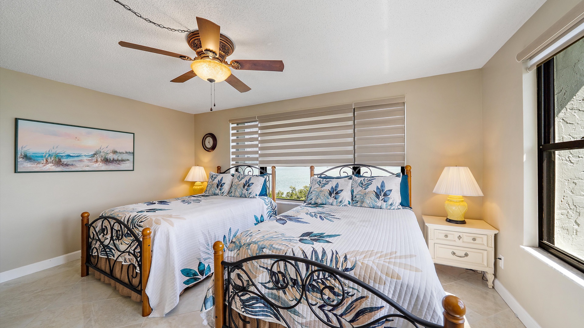 Relax in your peaceful twin bedroom with ocean-themed bedding, gentle ceiling fan, and soothing natural light for restful nights.