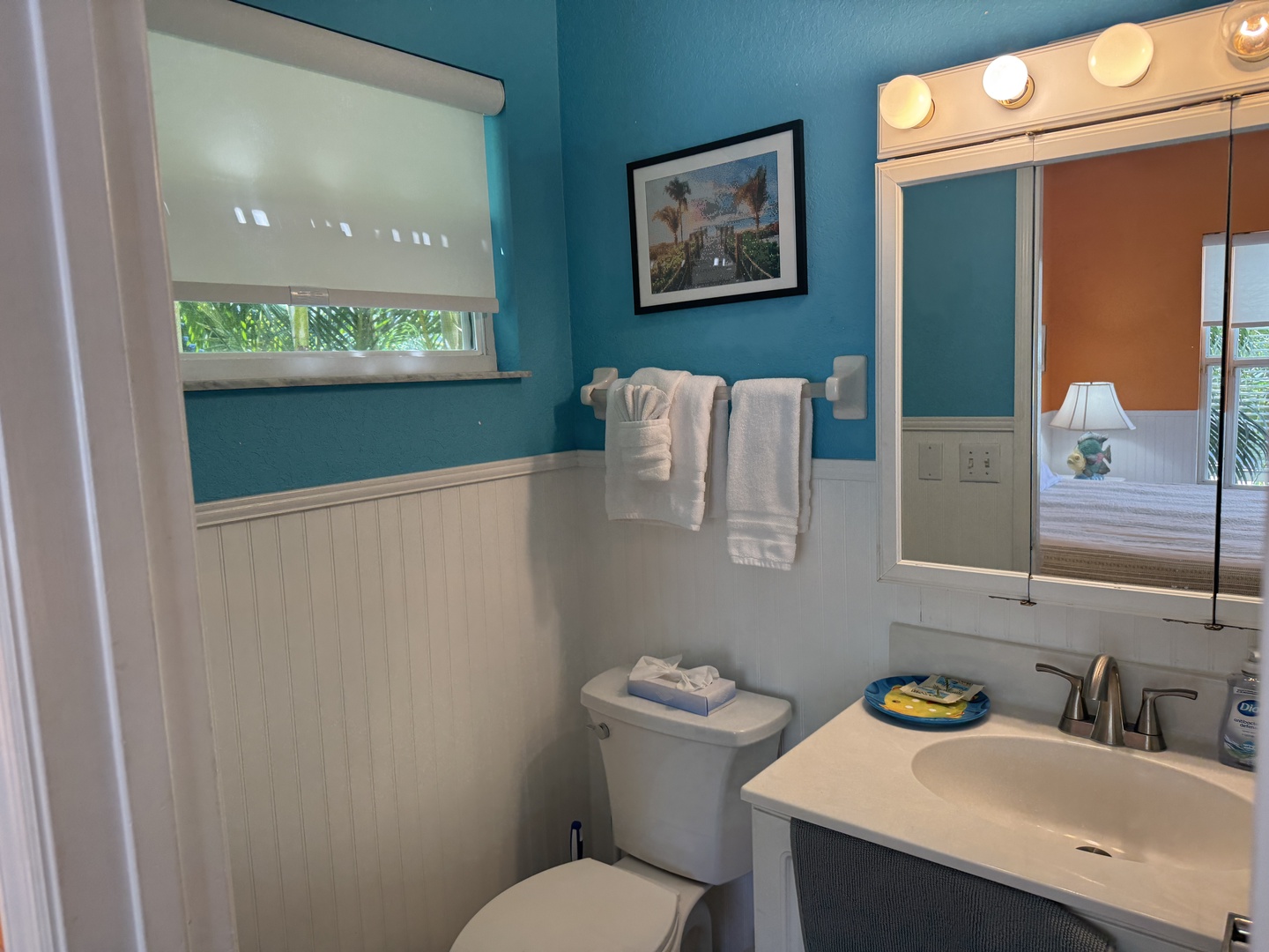 Step into your freshly updated bathroom, where vibrant turquoise walls meet coastal charm. Fresh towels await, vanity lighting sets a warm glow, and every detail invites you to unwind in comfort.