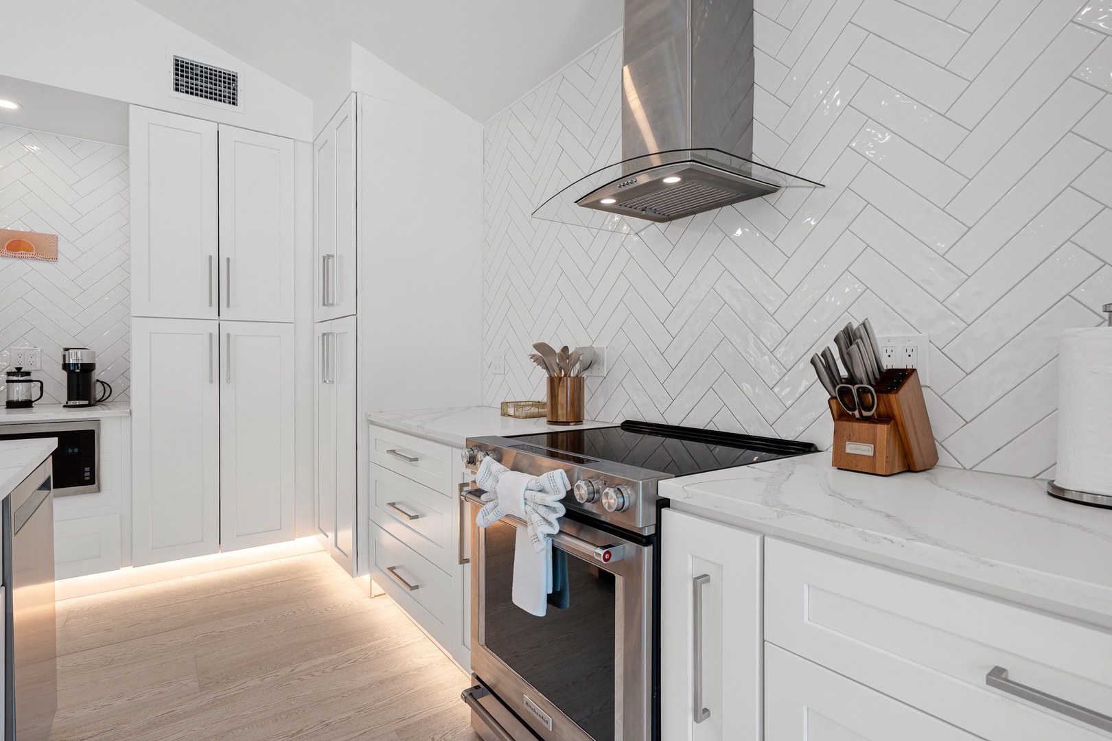 Your gourmet kitchen awaits with sleek stainless appliances, stylish herringbone backsplash, and elegant white cabinetry bathed in soft ambient lighting—perfect for creating memorable meals during your stay.