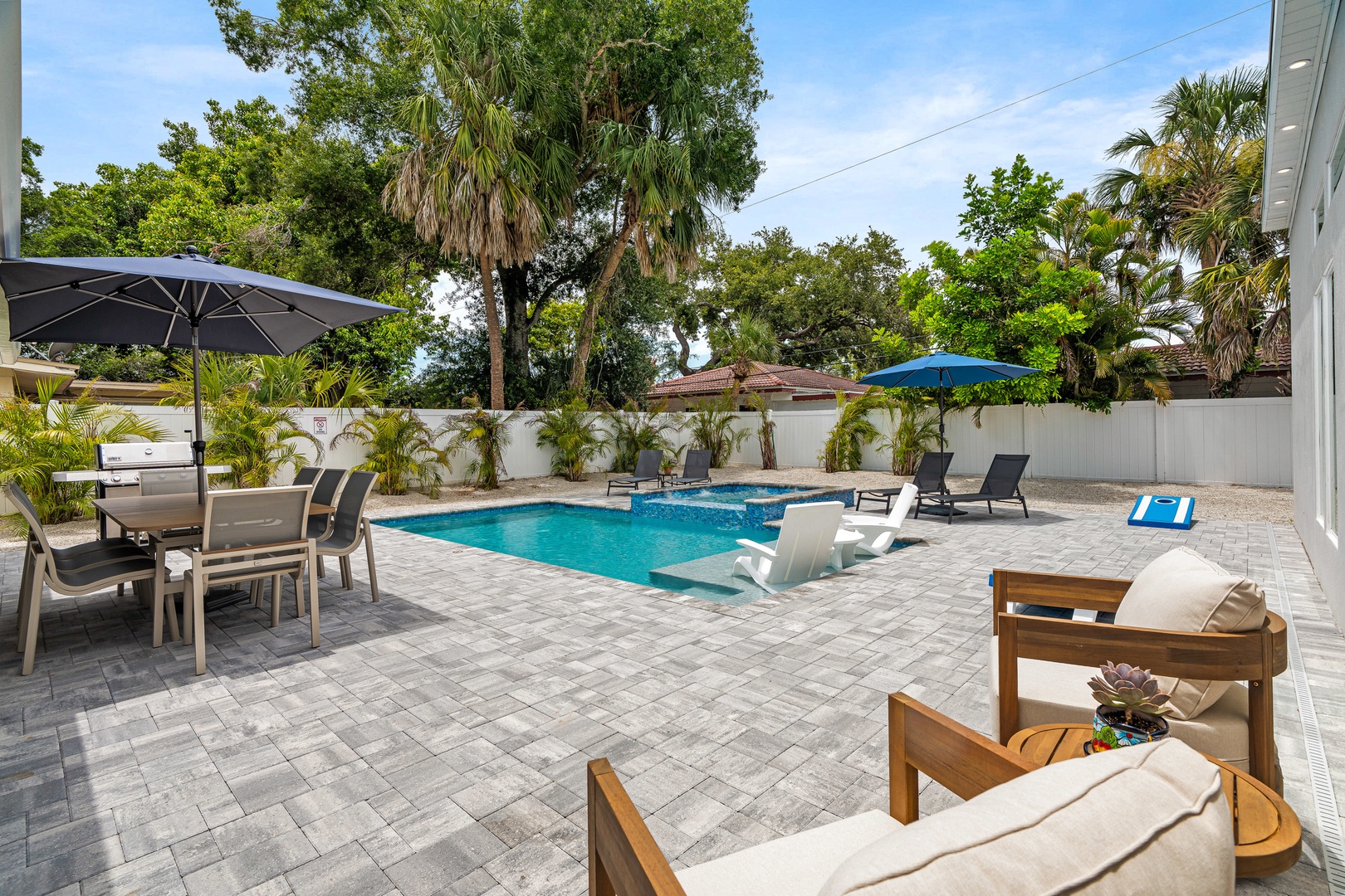 Spacious pool deck with ample lounge chairs, covered dining area, outdoor grill and corn hole game.