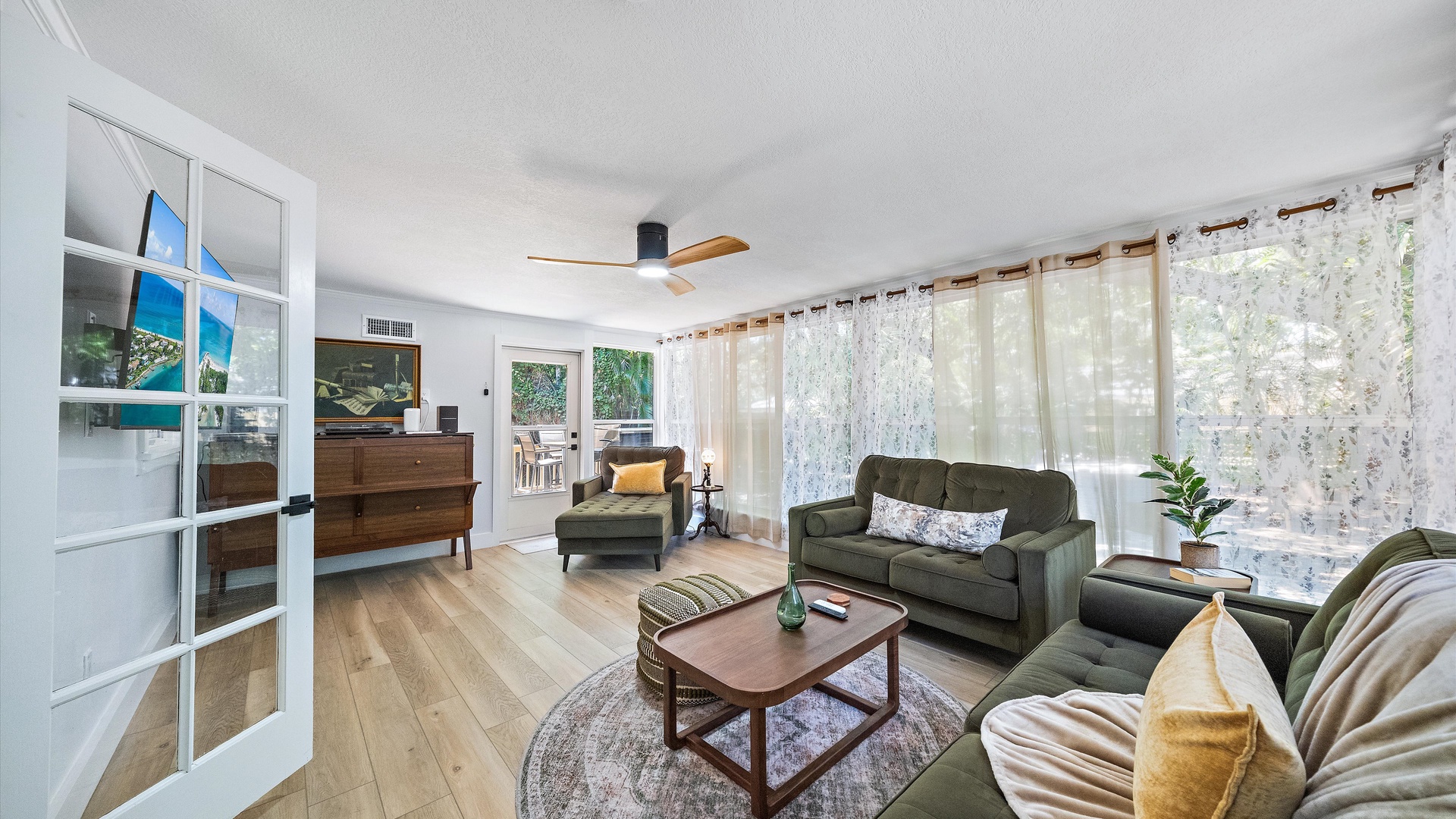 Sink into plush sofas in your sun-dappled living room, where natural light pours through sheer curtains and a ceiling fan keeps the air fresh. The space feels open, inviting, and ready for your next relaxing afternoon.