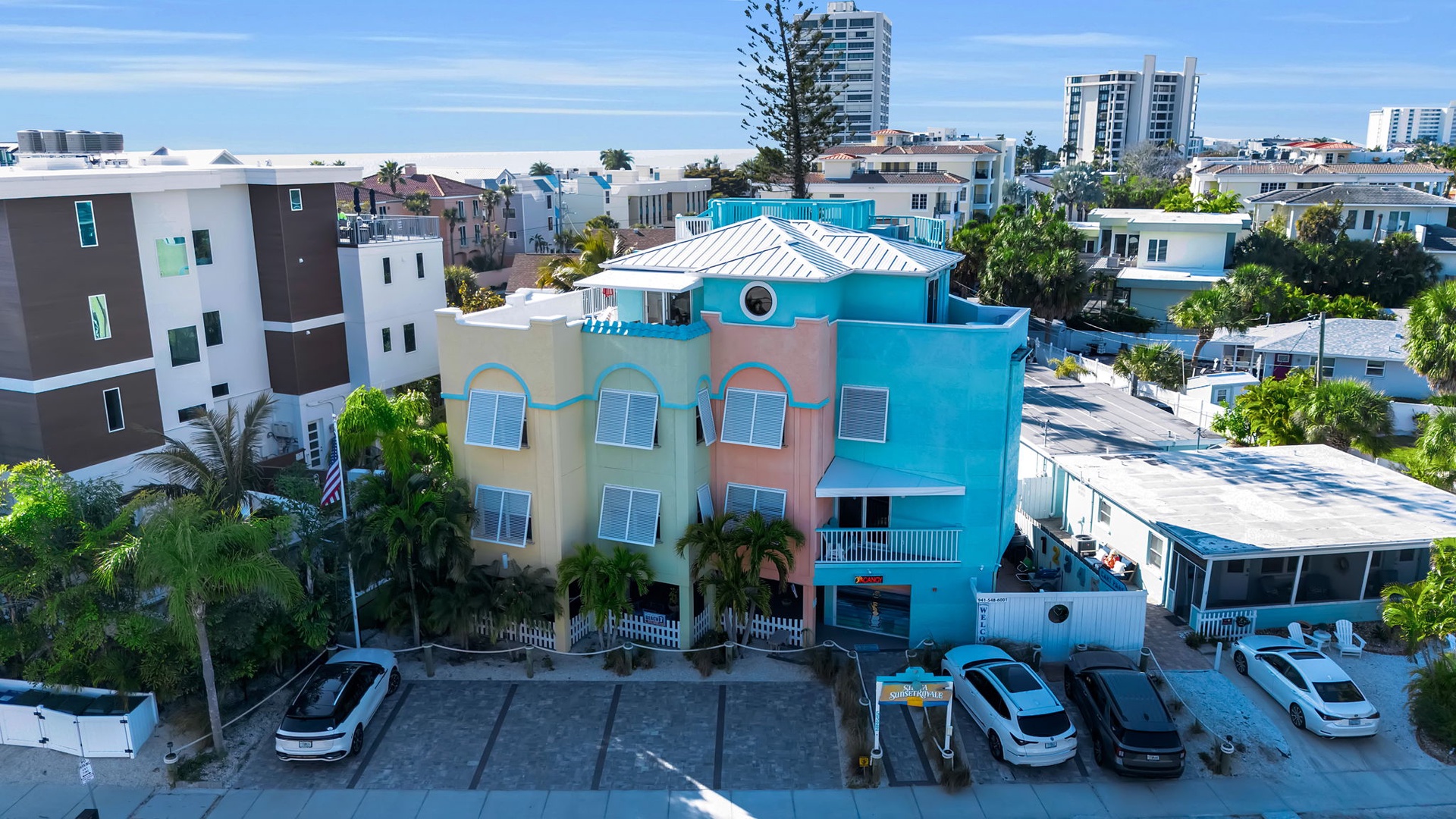 The vibrant beachside property stands out with colorful architecture and convenient parking in a sunny coastal neighborhood with palm-lined streets and nearby beach access.