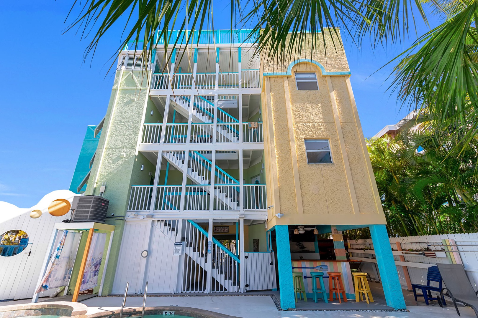 A colorful beachside property with vibrant turquoise and yellow accents, surrounded by swaying palms under a clear blue sky.