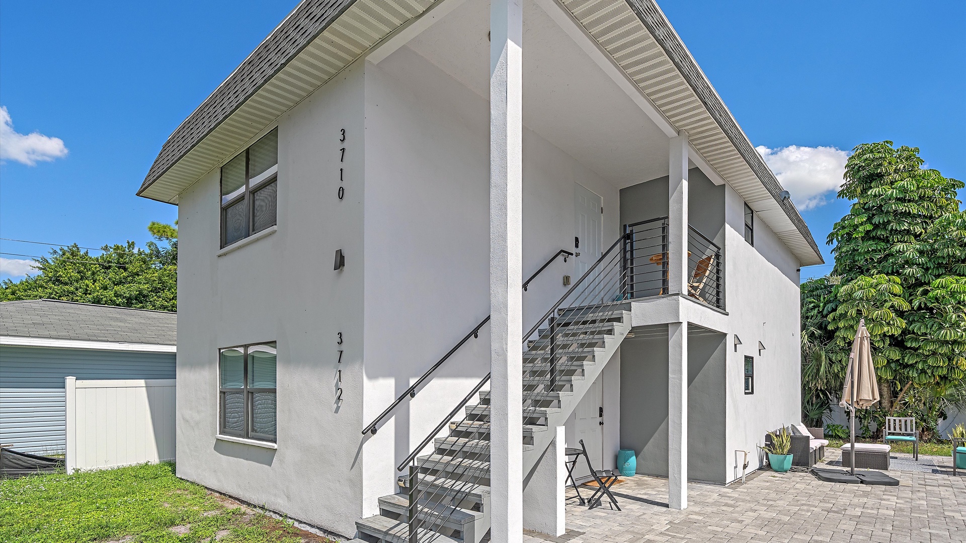 Modern two-story property featuring clean architectural lines and covered outdoor spaces, set in a peaceful neighborhood surrounded by lush tropical greenery.