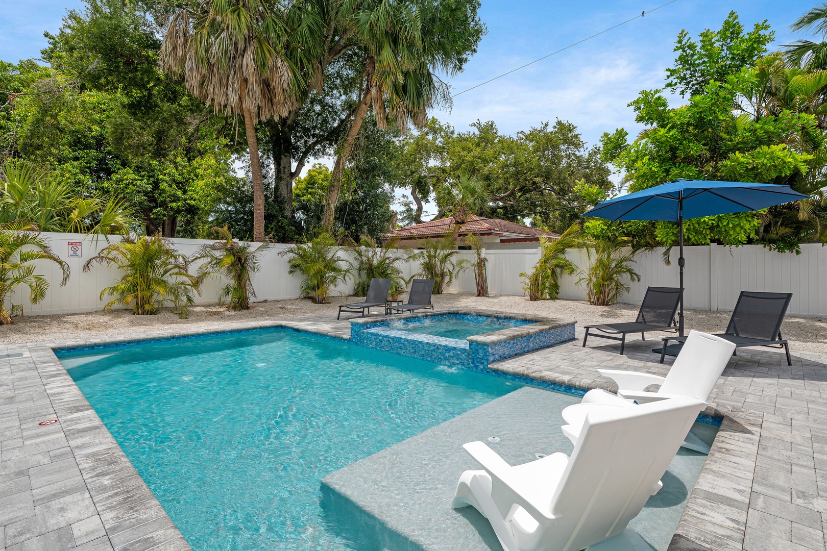 Spacious pool deck with ample lounge chairs, covered dining area, outdoor grill and corn hole game.