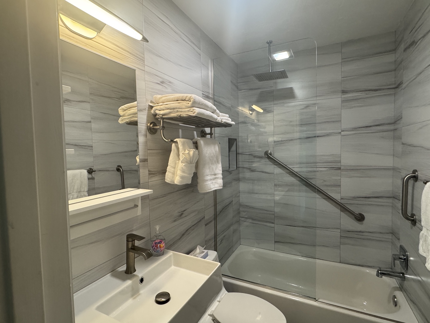 Step into your sleek bathroom with modern gray tile, a full-size tub and shower combo, and fresh towels waiting for you. Clean lines and thoughtful touches make this space feel both stylish and practical for your stay.