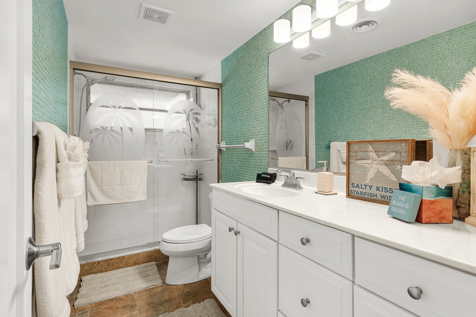 Refresh in your coastal-inspired bathroom featuring bright turquoise tile, a modern glass shower, and beach-themed touches that set a relaxed vacation mood.