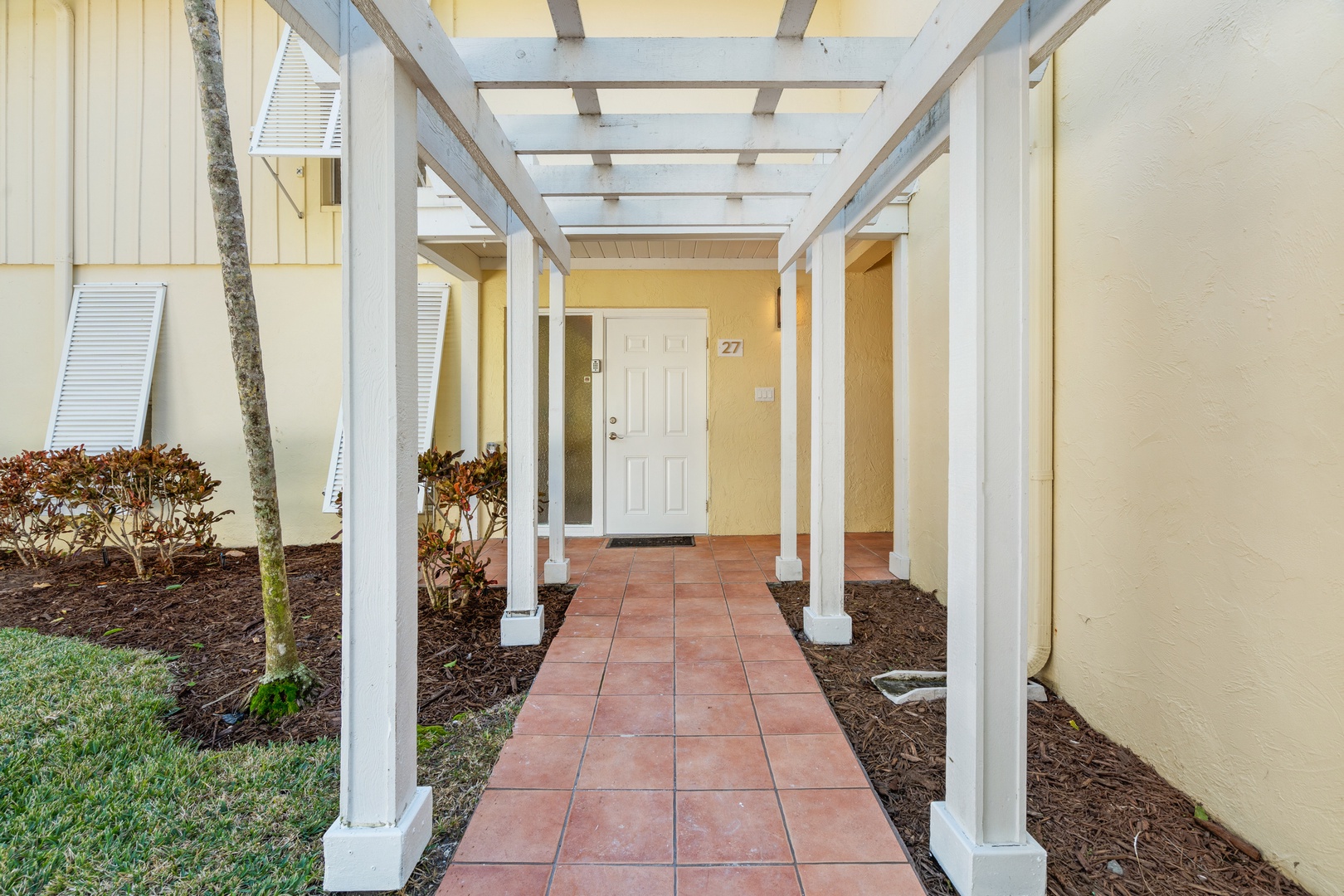 A welcoming covered walkway leads you to your private entrance, framed by clean white columns and landscaped gardens.
