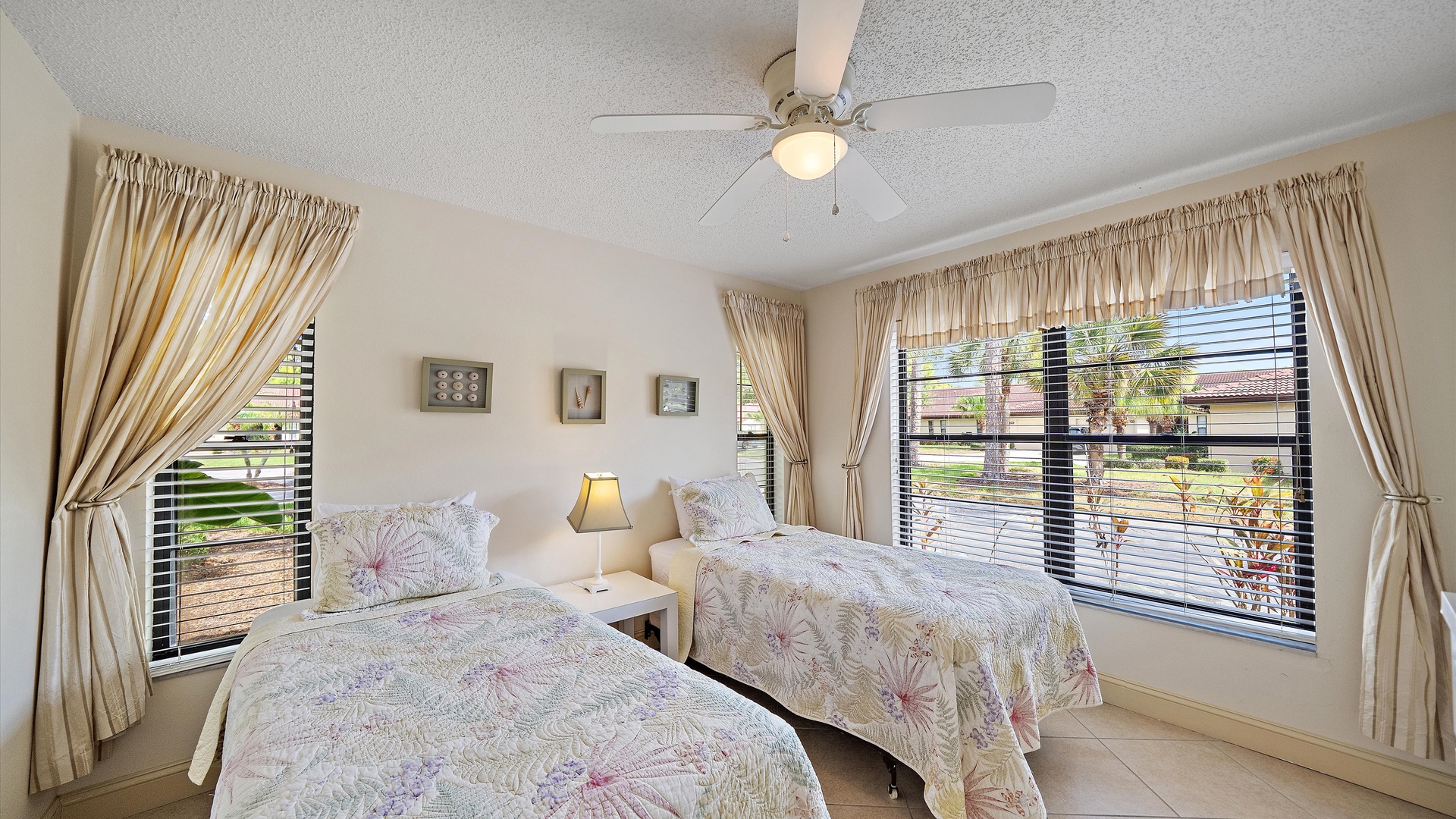 You'll rest easy in this peaceful bedroom with two twin beds dressed in soft floral linens, elegant curtains framing garden views, and a ceiling fan keeping you comfortable throughout your stay.