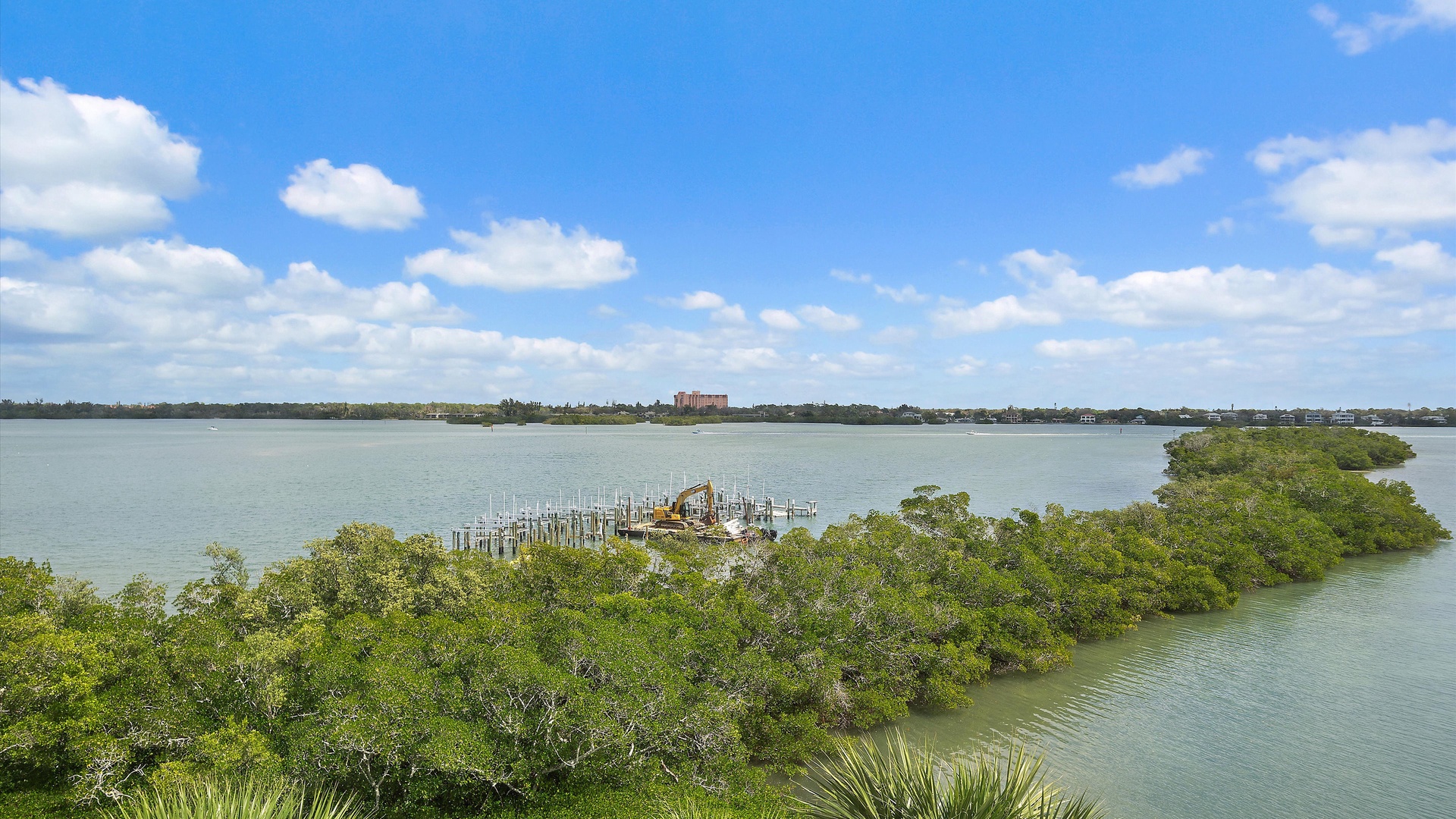 Expansive waterfront vista showcases pristine coastal waters, lush mangrove islands, and distant development under brilliant blue skies.