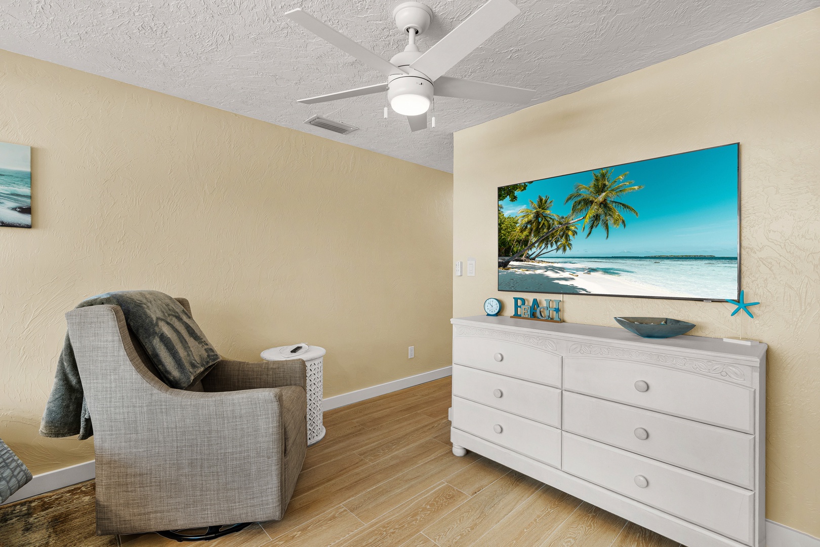 The cozy bedroom features warm tones, hardwood floors, and a ceiling fan to keep you comfortable during your stay. Relax in the armchair after a day of exploring or settle in for a peaceful night's rest.