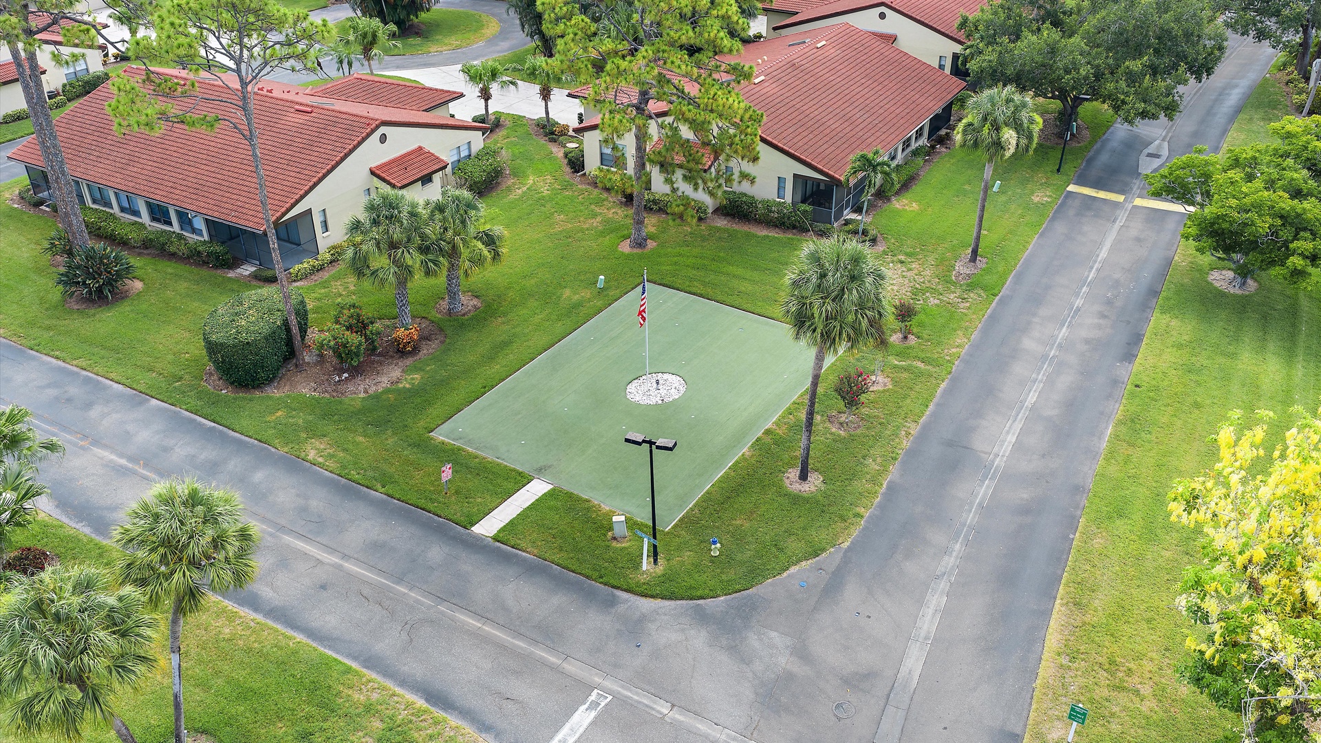 Aerial view of a peaceful residential property featuring Mediterranean-style buildings with red-tiled roofs, lush landscaped grounds with palm trees, and a dedicated putting green for golf enthusiasts.