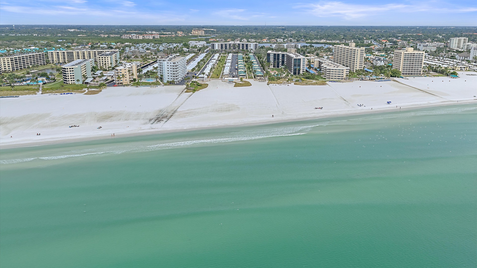 Aerial view of the coastal area featuring pristine white sand beaches along the Gulf of Mexico, with resort hotels and condominiums lining the shoreline.