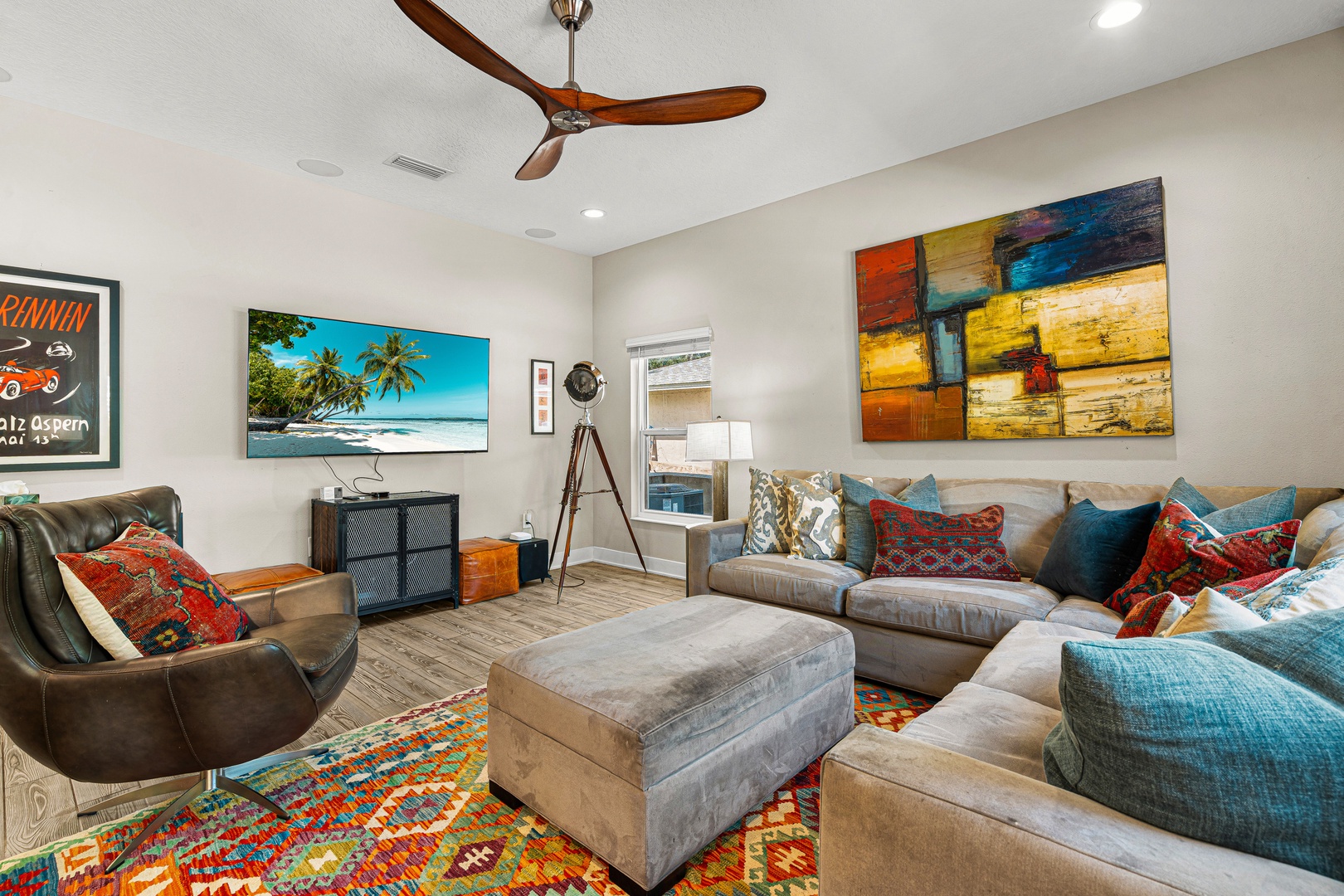 Sink into plush sectional seating surrounded by vibrant art and eclectic décor. The open layout invites you to unwind beneath the ceiling fan's gentle breeze, while natural light and thoughtful design create a warm, effortlessly stylish retreat.