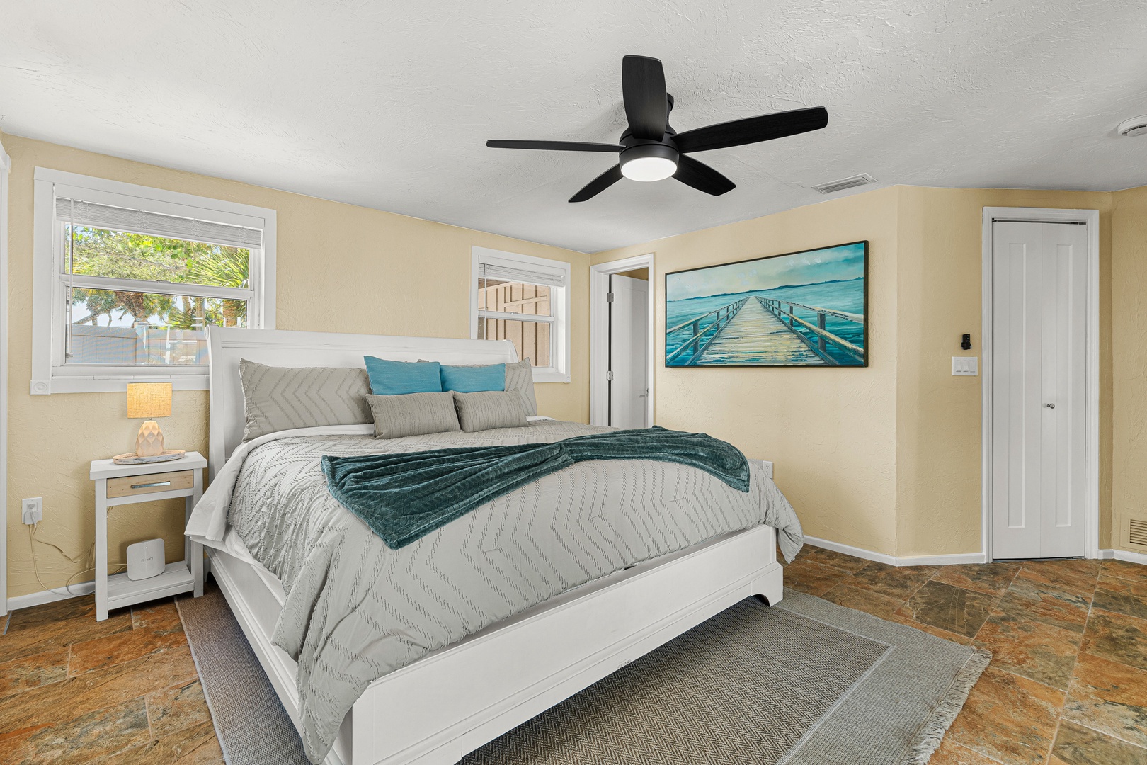 Sink into your plush bed under gentle ceiling fan breezes, where soft coastal tones and natural light create your peaceful retreat.