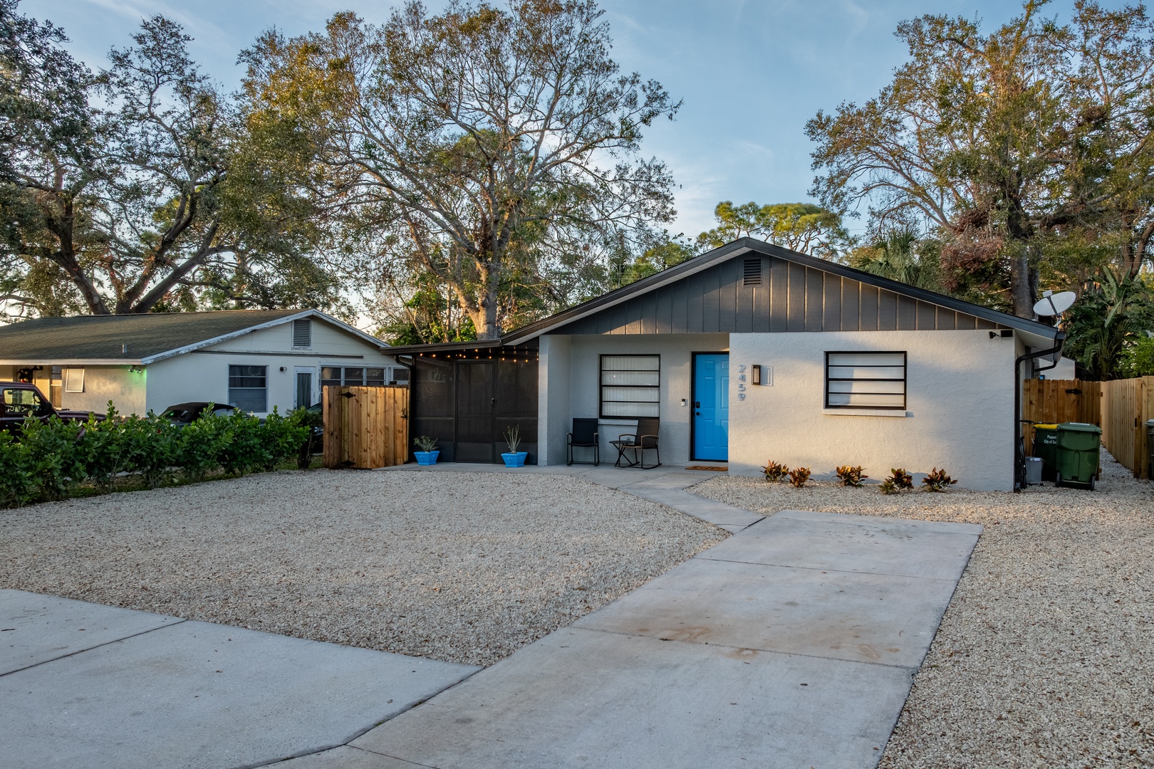 Modern property featuring bright blue entrance door, private driveway, and mature tree-lined surroundings creating a peaceful neighborhood setting.