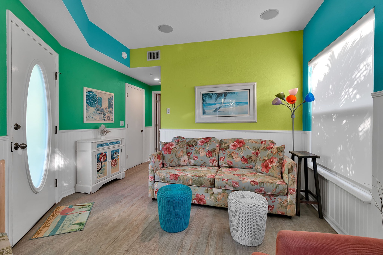 Step into a cheerful tropical retreat with vibrant turquoise and lime walls, a cozy floral sofa, and beachy accents that instantly make you feel relaxed and at home.