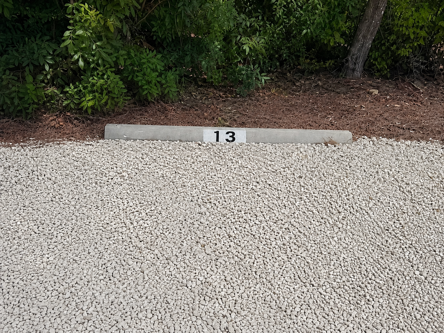 Parking spot 13 is located in a gravel area surrounded by natural landscaping and greenery.