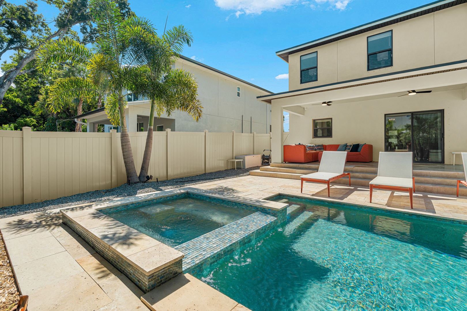 Modern two-story property with private pool, integrated hot tub, and covered patio framed by tropical palm trees under clear blue skies.