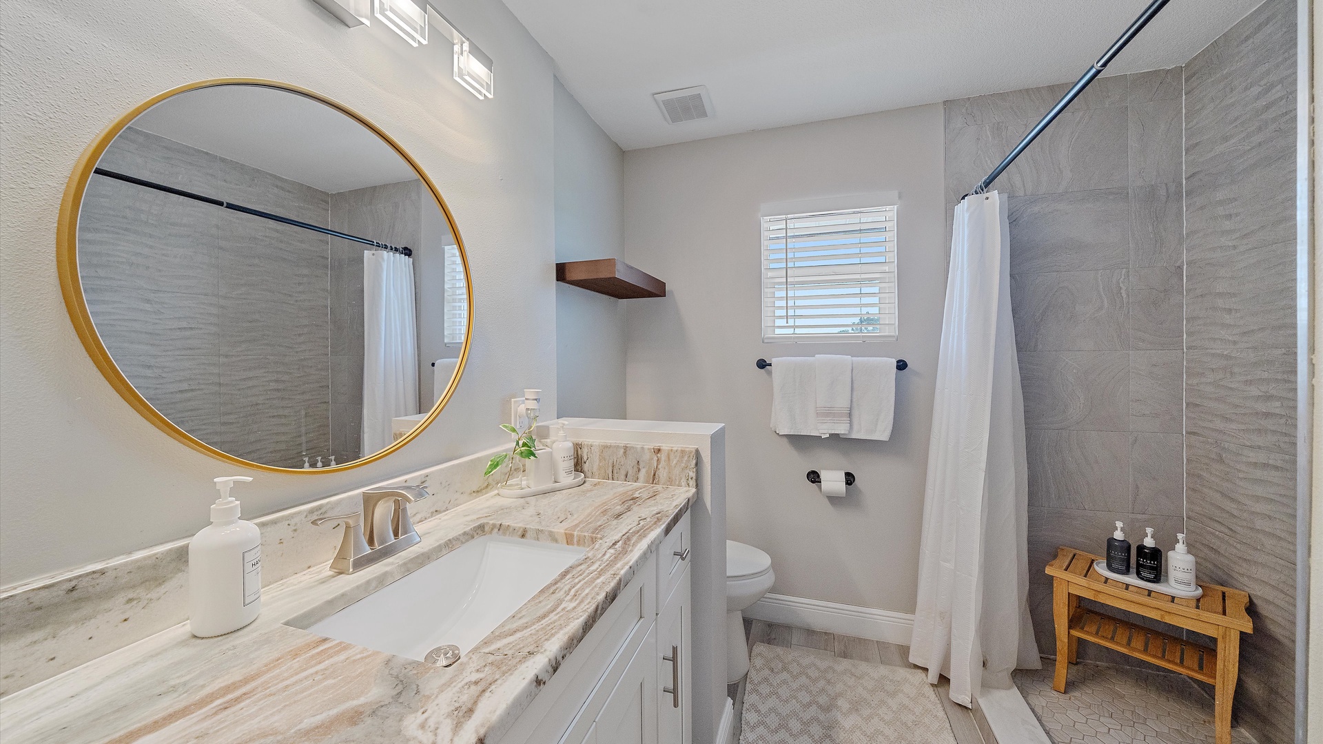 Your private bathroom is beautifully designed with elegant marble countertops, a warm gold-framed mirror, and a spacious walk-in shower with fresh white linens waiting for you.