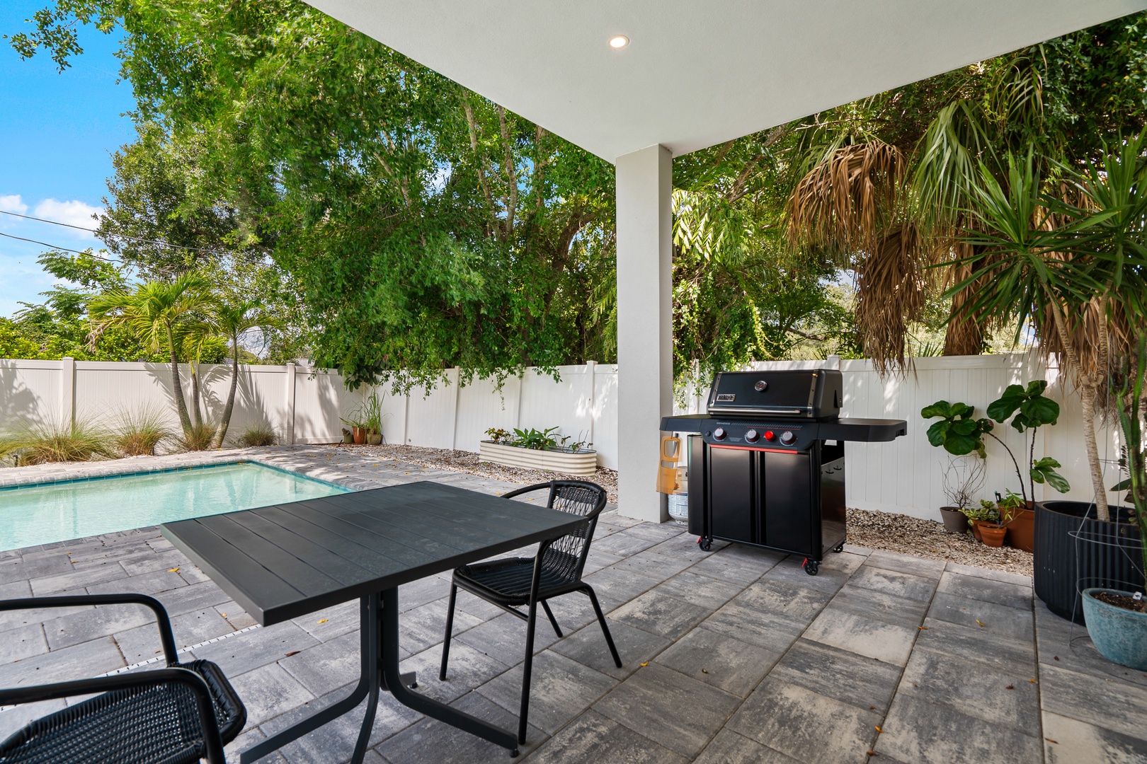 Your private covered patio overlooks a sparkling pool and lush tropical greenery, complete with a BBQ grill ready for sunset cookouts under the palms.