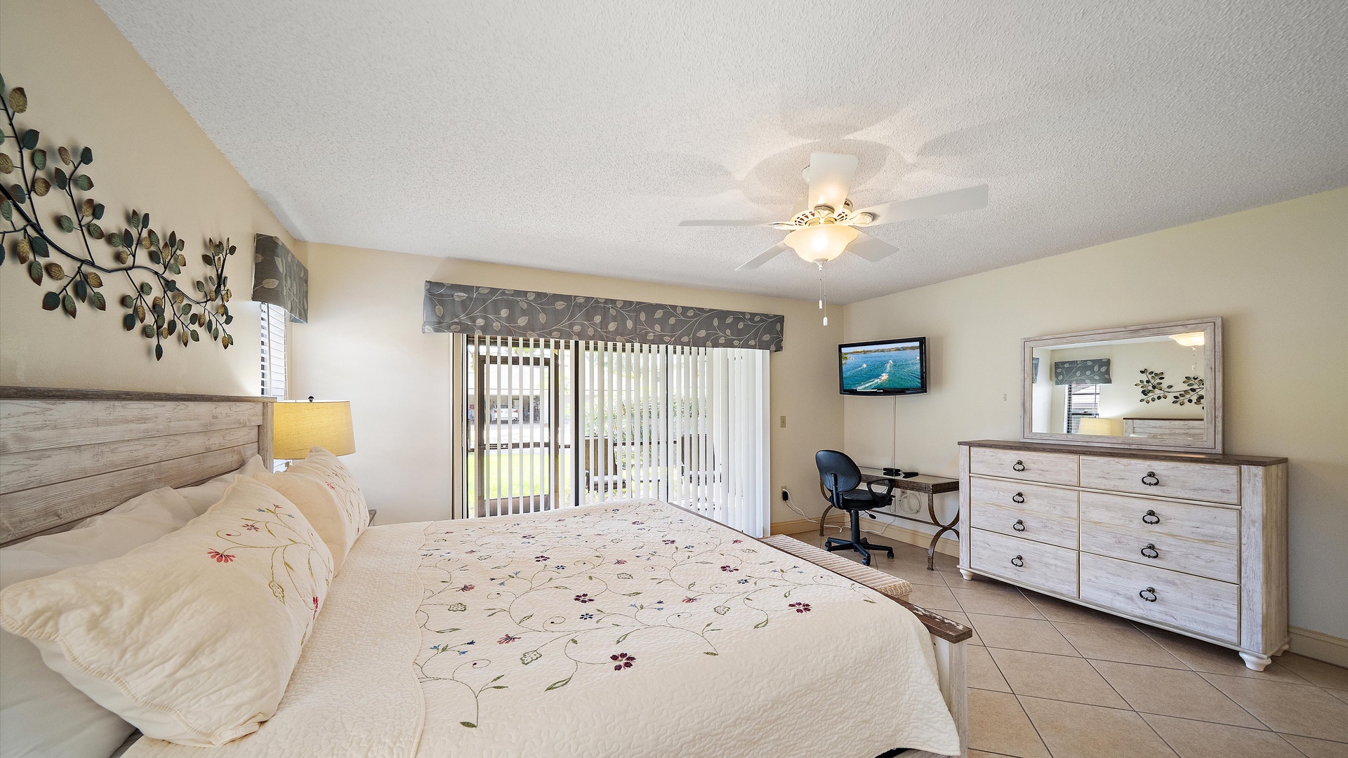 Your peaceful bedroom features a plush bed, calming coastal tones, ceiling fan, flat-screen TV, dresser, workspace, and sliding doors that open to natural light.