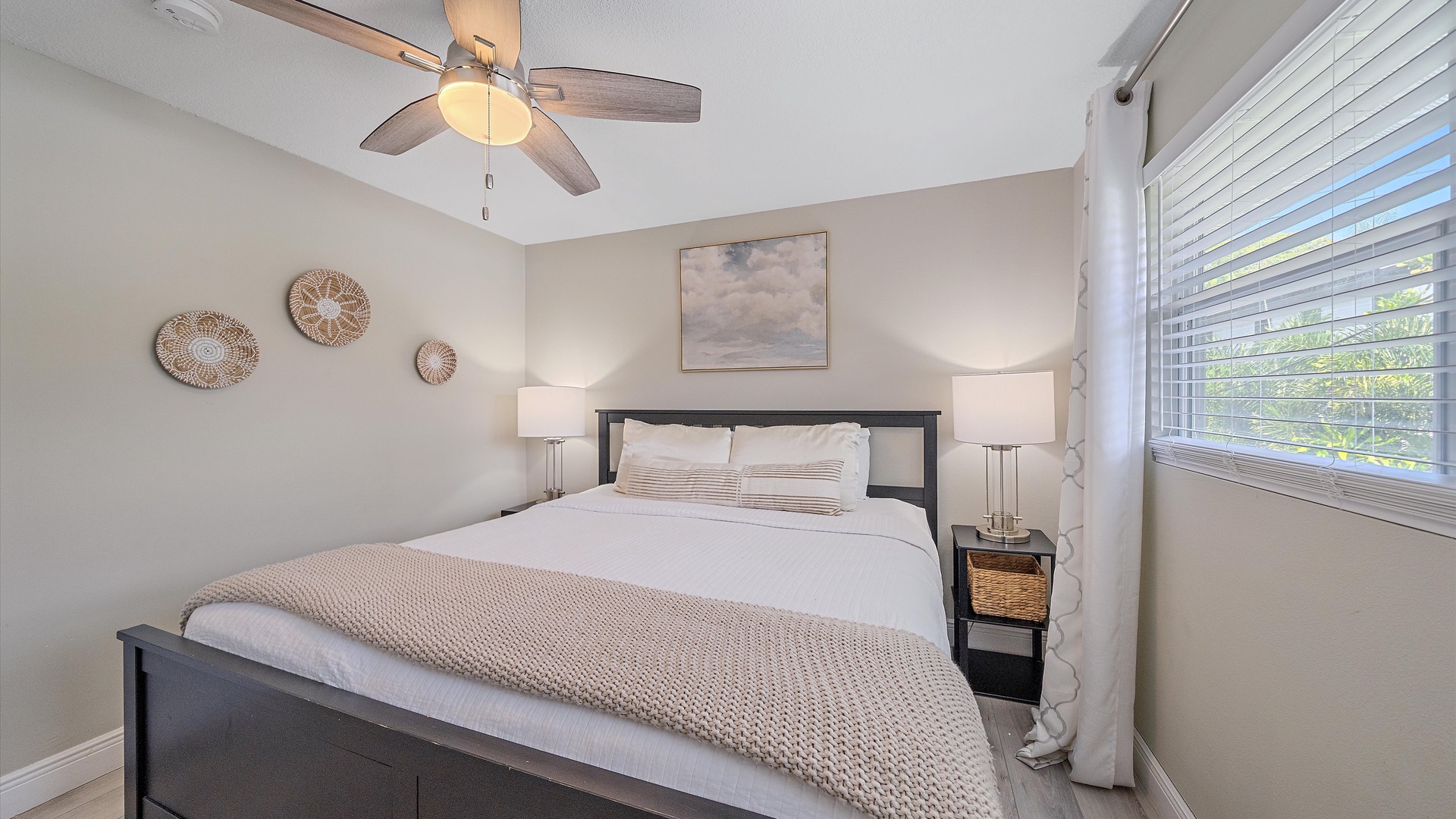 Sink into plush white linens and let the gentle ceiling fan breeze lull you to sleep in this serene coastal-inspired bedroom, designed for your ultimate comfort.