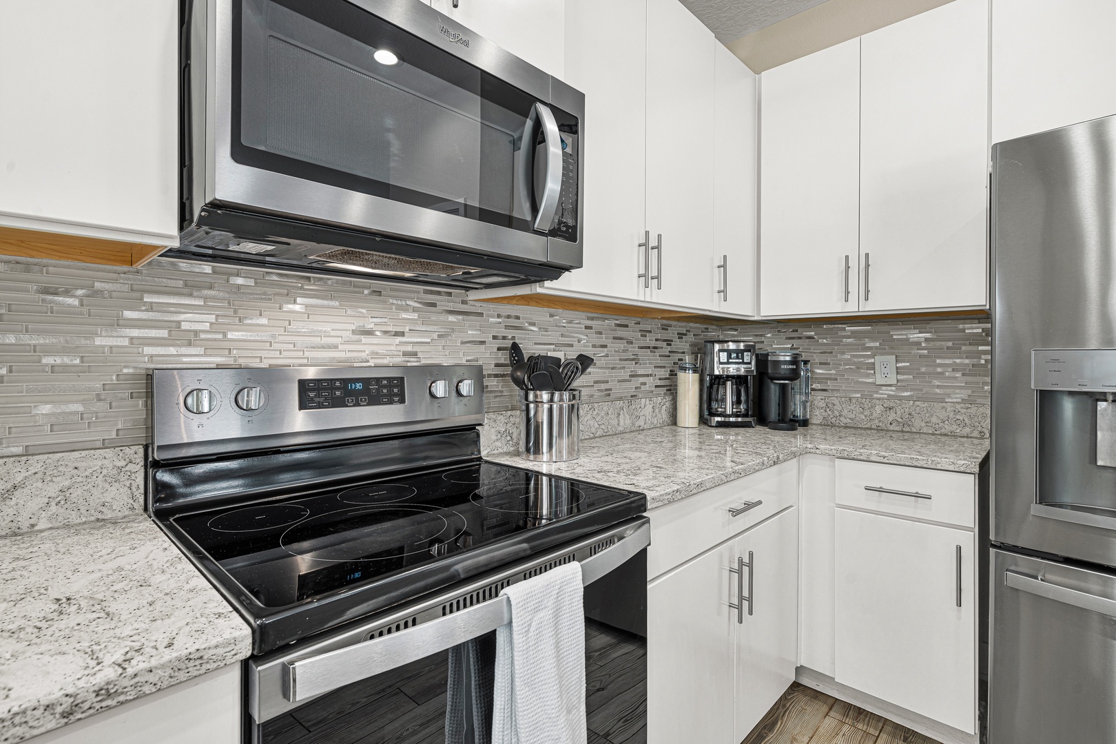 Your fully equipped kitchen features stainless steel appliances, granite countertops, and a stylish glass tile backsplash, ready for preparing your favorite meals and morning coffee.