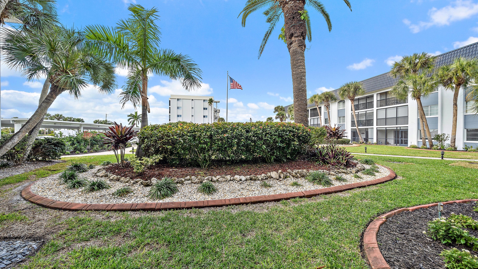 Tropical resort grounds feature manicured landscaping with palm trees and colorful plantings surrounding modern vacation rental buildings.