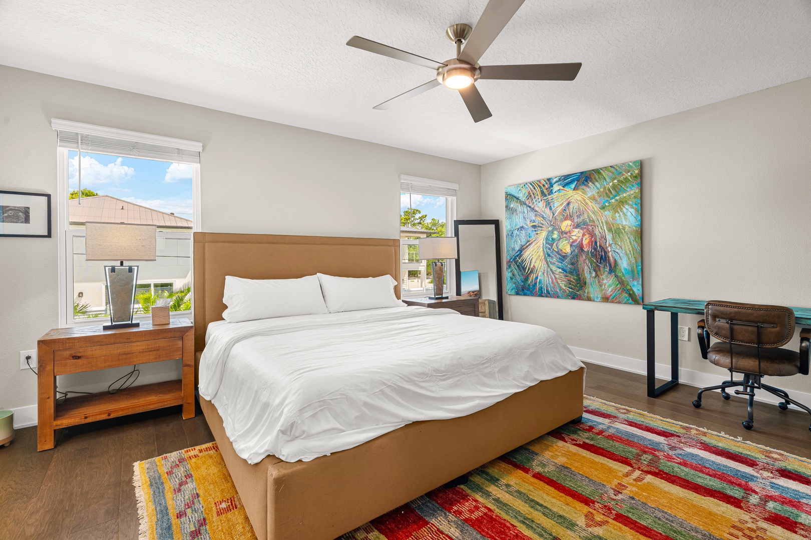 Drift off under the gentle breeze of the ceiling fan in your cozy retreat. Natural light fills the room through bright windows, while tropical artwork adds a vibrant coastal touch to your peaceful escape.