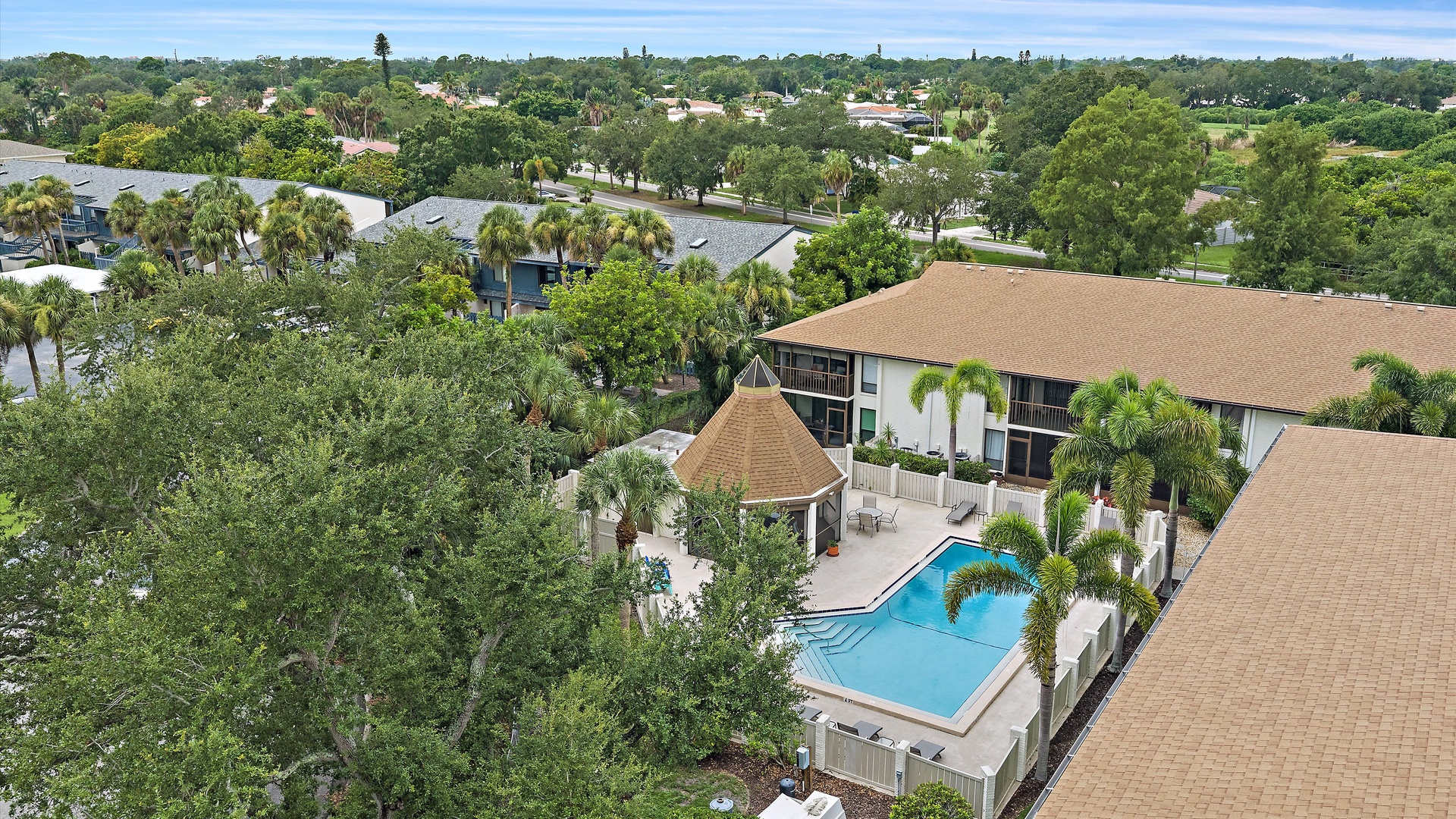 Aerial perspective of the property complex, showcasing the pool area and surrounding residential neighborhood in a lush, tropical setting.