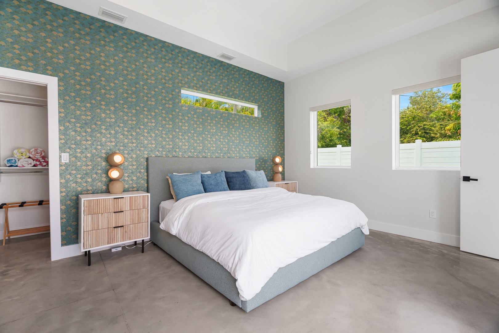 Unwind in your serene bedroom featuring a plush bed, charming accent wall, and bright windows overlooking lush greenery. Your restful retreat awaits.