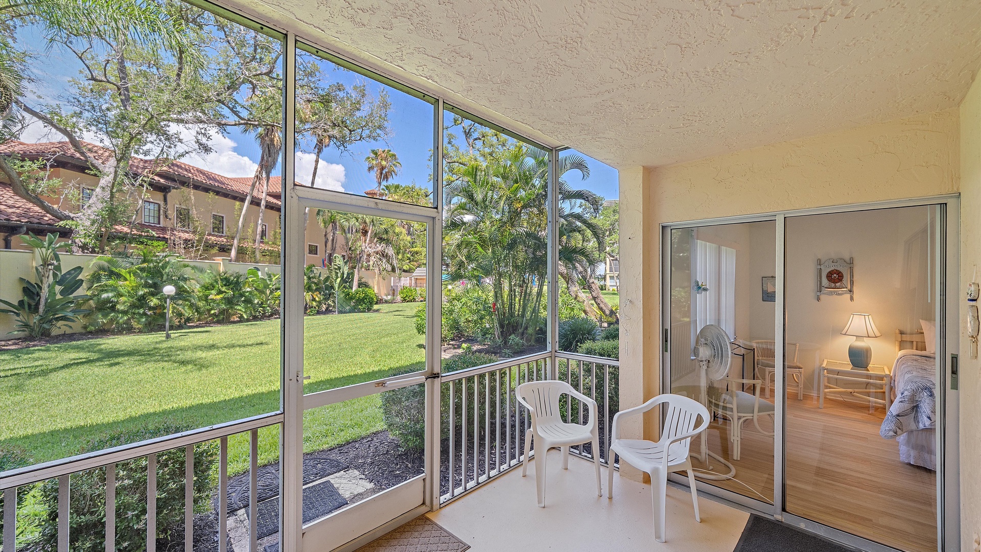 Your private screened-in porch overlooks lush tropical gardens with palm trees, offering a peaceful spot to relax in your outdoor chairs while enjoying resort grounds views.