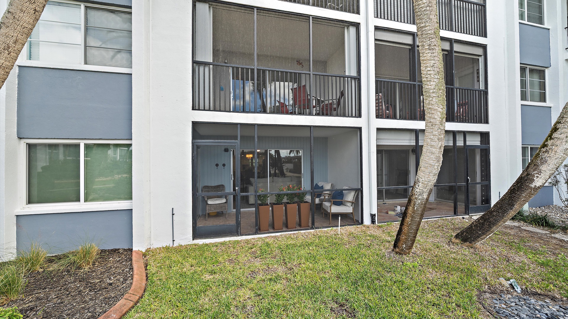 Modern condo building with sliding glass doors opening to private outdoor spaces and tropical landscaping.