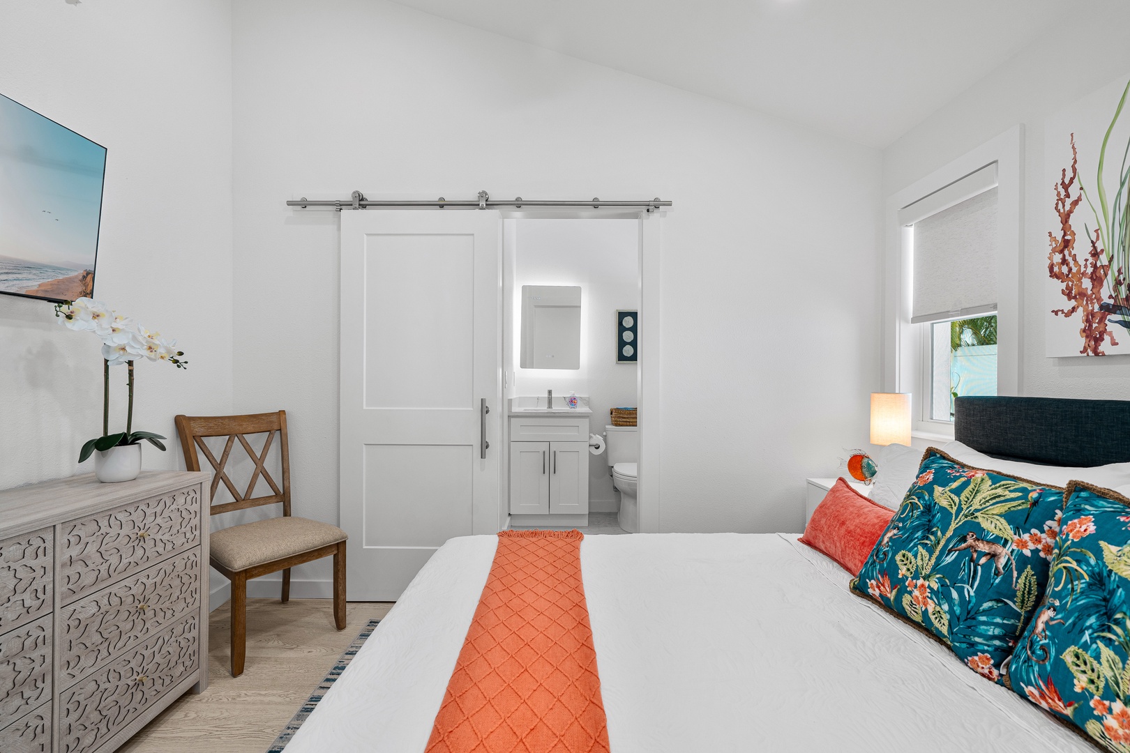 Your bright, airy bedroom features a plush king bed with vibrant tropical accents, an elegant sliding barn door to your private en-suite bath, and thoughtful touches like fresh orchids welcoming you home.