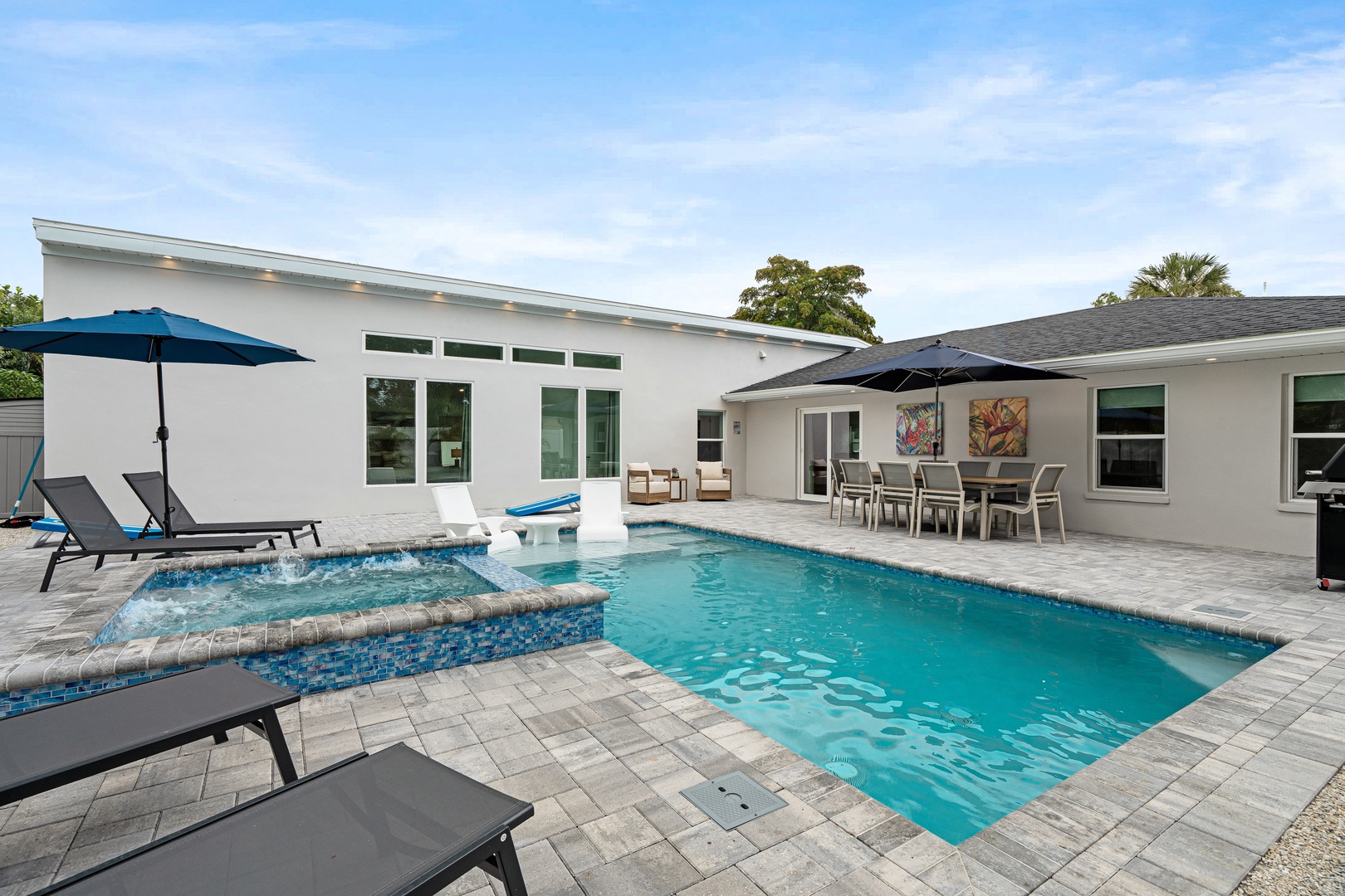 Spacious pool deck with ample lounge chairs, covered dining area, outdoor grill and corn hole game.