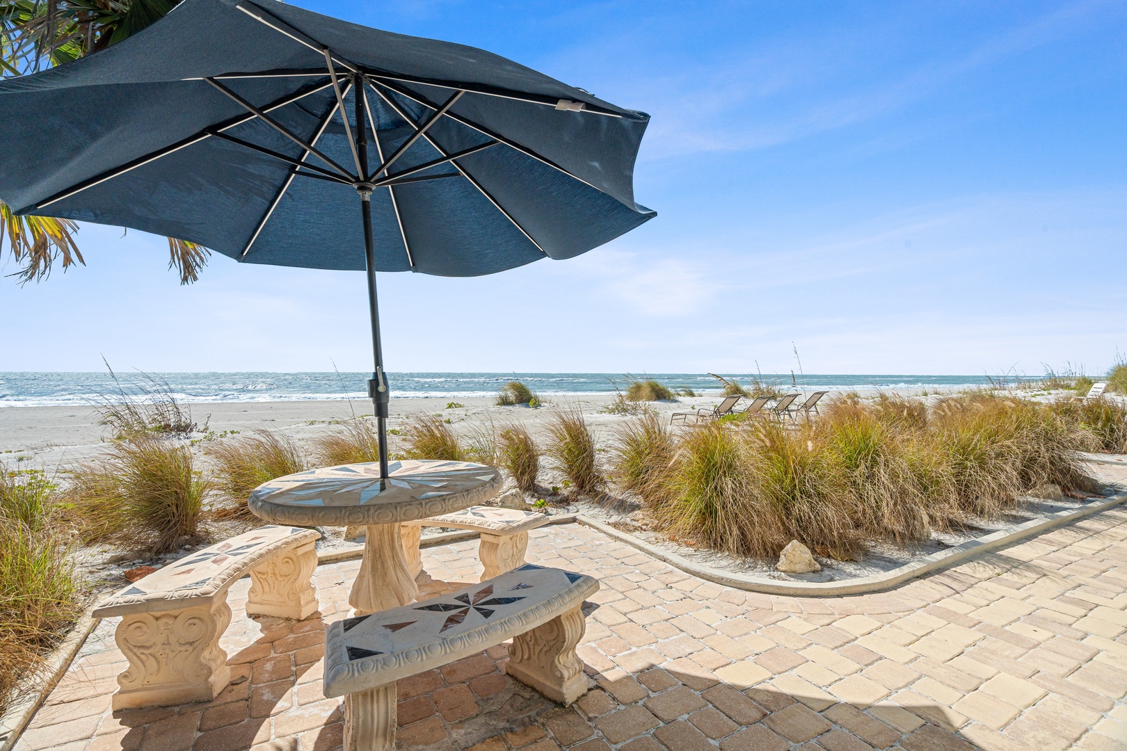 Beachfront seating area with umbrella shade and ocean views, featuring natural dune landscaping.
