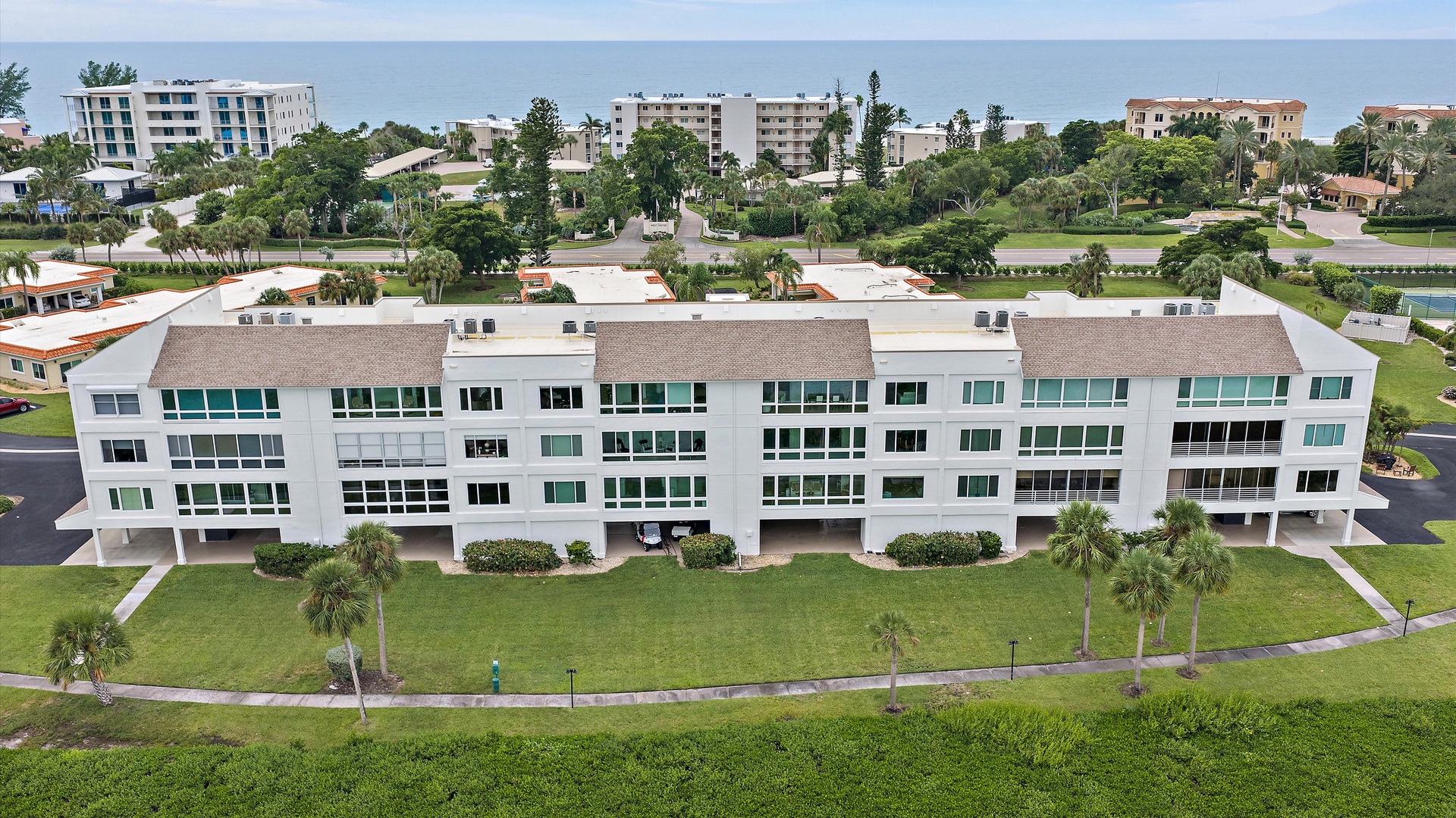 A waterfront-side view of the building, with broad windows facing the bay and green grounds below. The penthouse’s enclosed sunroom makes the most of this appealing orientation.