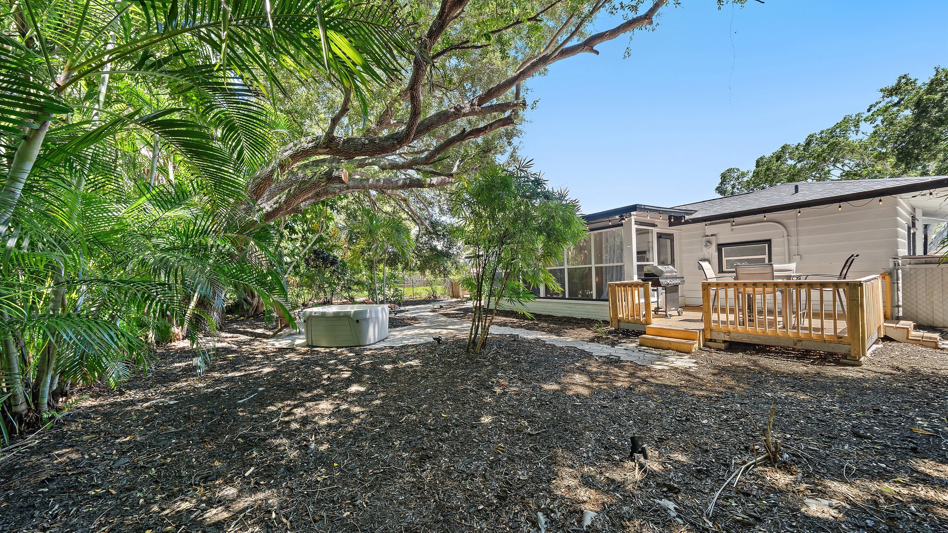 Your private outdoor retreat includes a relaxing hot tub and BBQ on a spacious deck, surrounded by lush tropical greenery and shaded by mature trees.