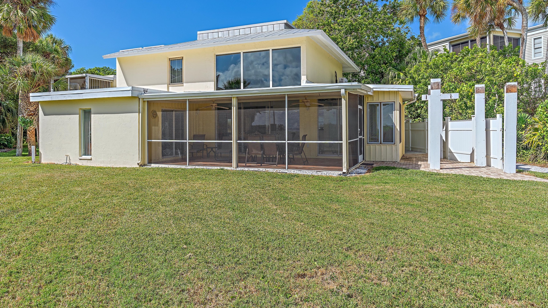 A two-story house with large windows, a screened-in porch, and a well-maintained lawn. Palm trees and lush greenery surround the property.
